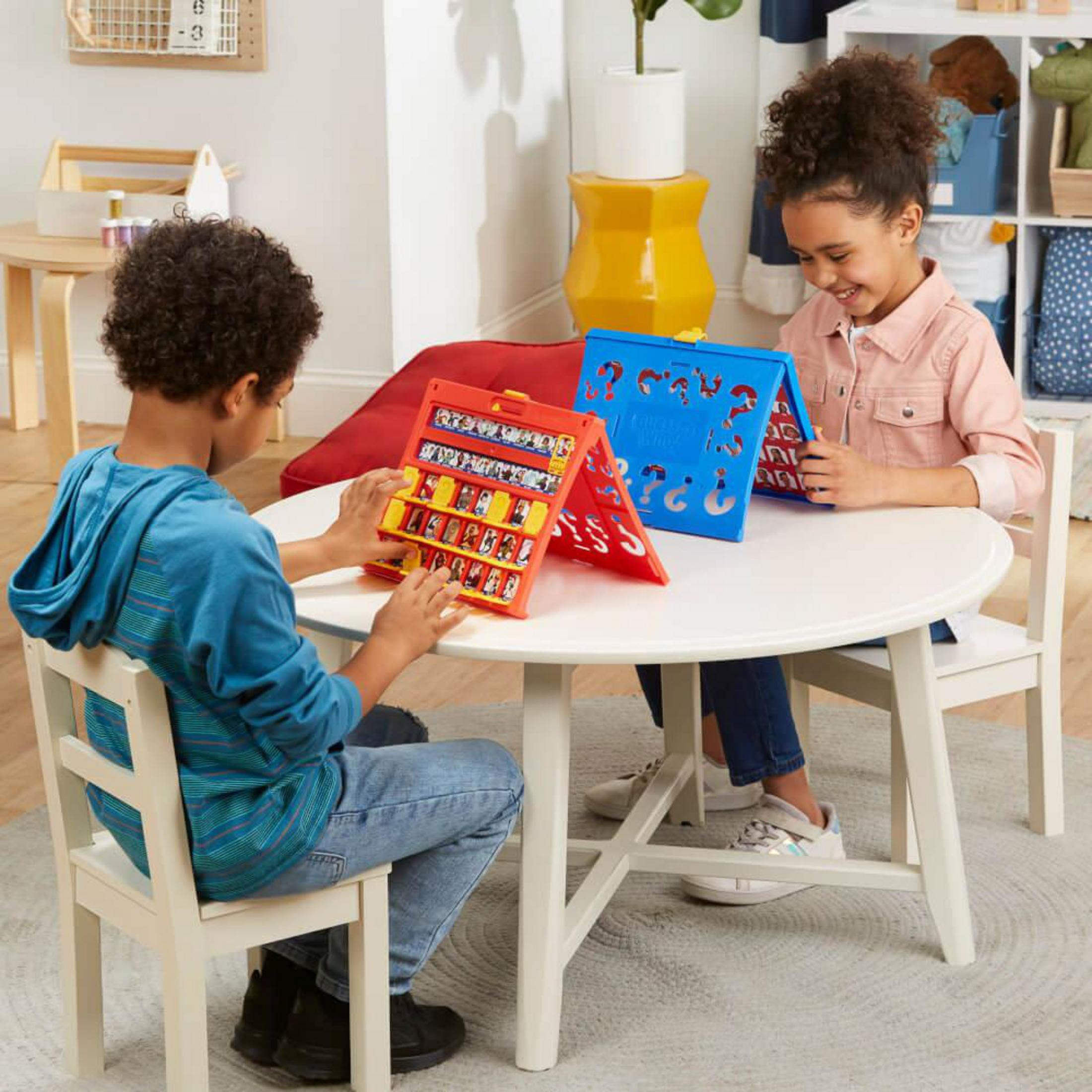 Due bambini giocano a Indovina Chi? Un bambino guarda il suo tabellone di gioco, sorridendo.
