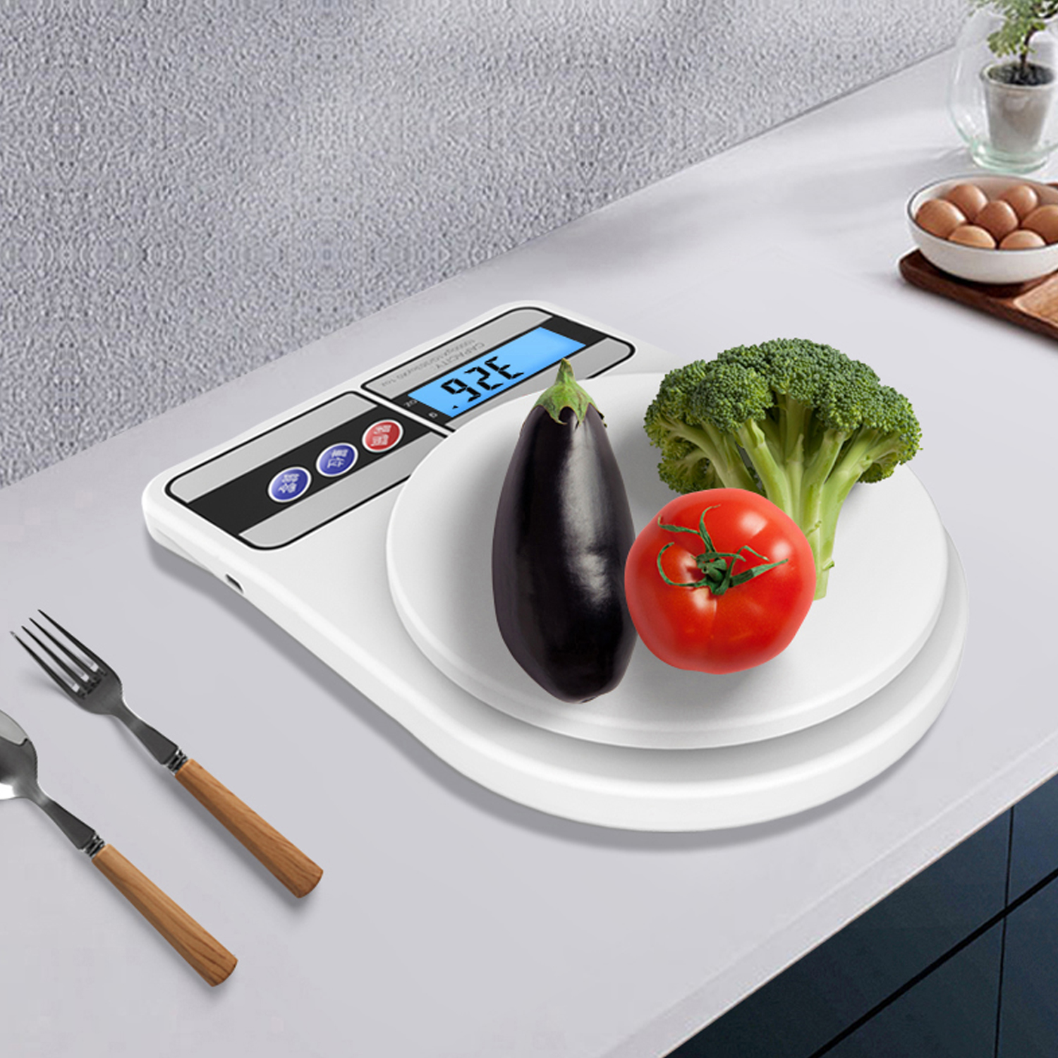 Digitale Küchenwaage mit einer Aubergine, Tomate und Brokkoli auf einem weißen Teller.