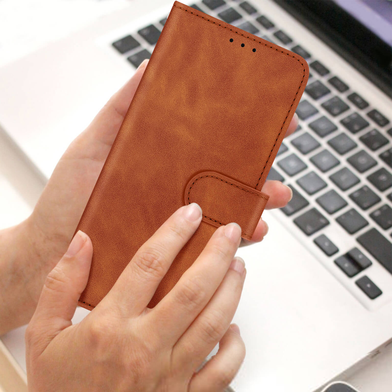 Un étui de téléphone en cuir marron est tenu au-dessus d'un clavier d'ordinateur portable. L'étui est fermé.