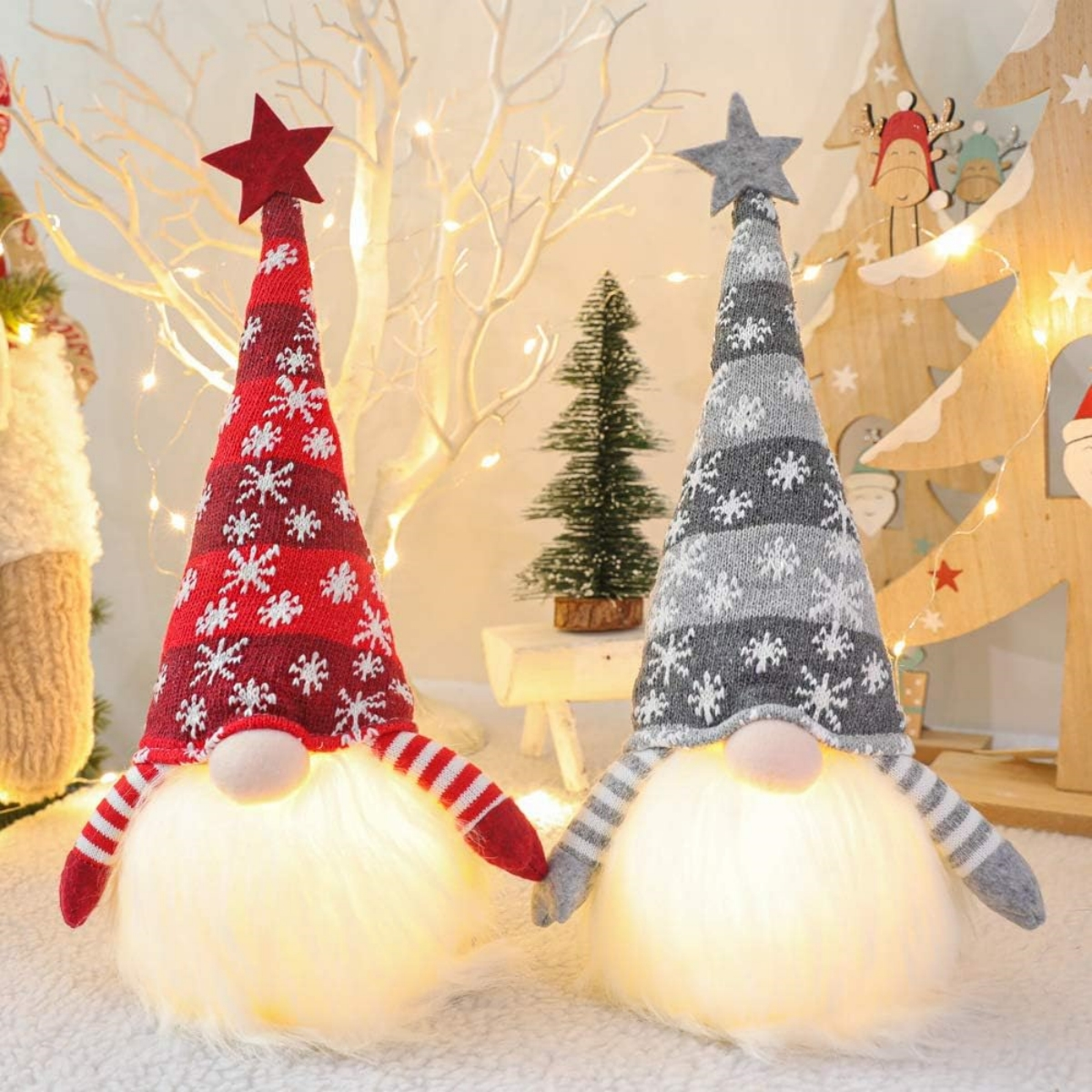 Zwei Weihnachtszwerge mit Sternhüten. Einer rot, einer grau. Lichter und Weihnachtsbaum im Hintergrund.