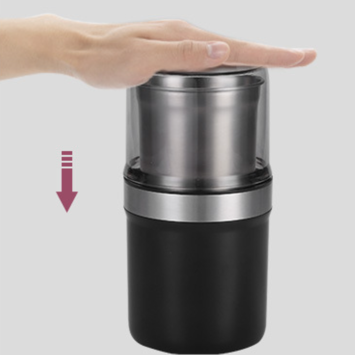 Hand drückt auf eine schwarze und silberne Kaffeemühle. Pfeil zeigt die Bewegung an.
