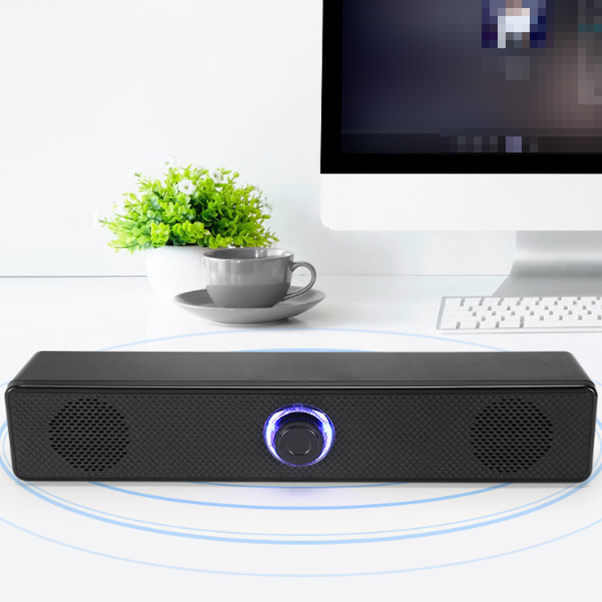 Schwarze Soundbar mit Lautstärkeregler, Lautsprechern und blauem Licht auf weißem Schreibtisch.