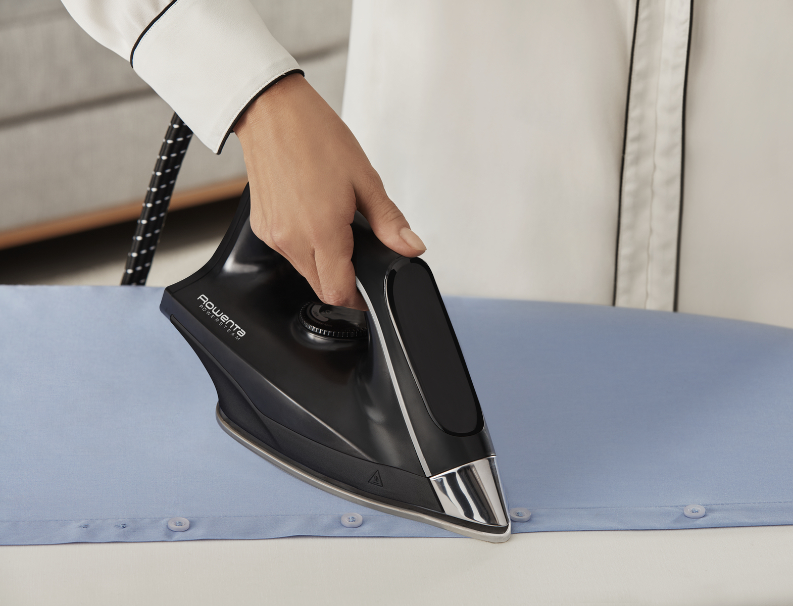 Una persona planchando una camisa azul claro con una plancha negra sobre una tabla de planchar.