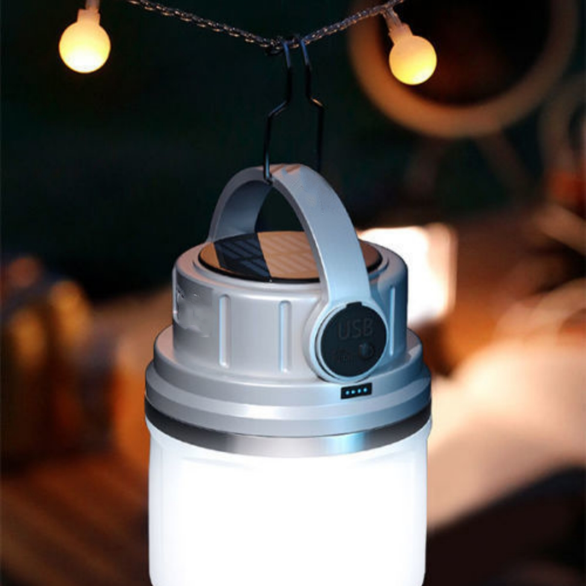 Eine silberne und weiße Laterne mit Griff, beleuchtet, hängt mit zwei kleinen Lichtern in verschwommenem Hintergrund.