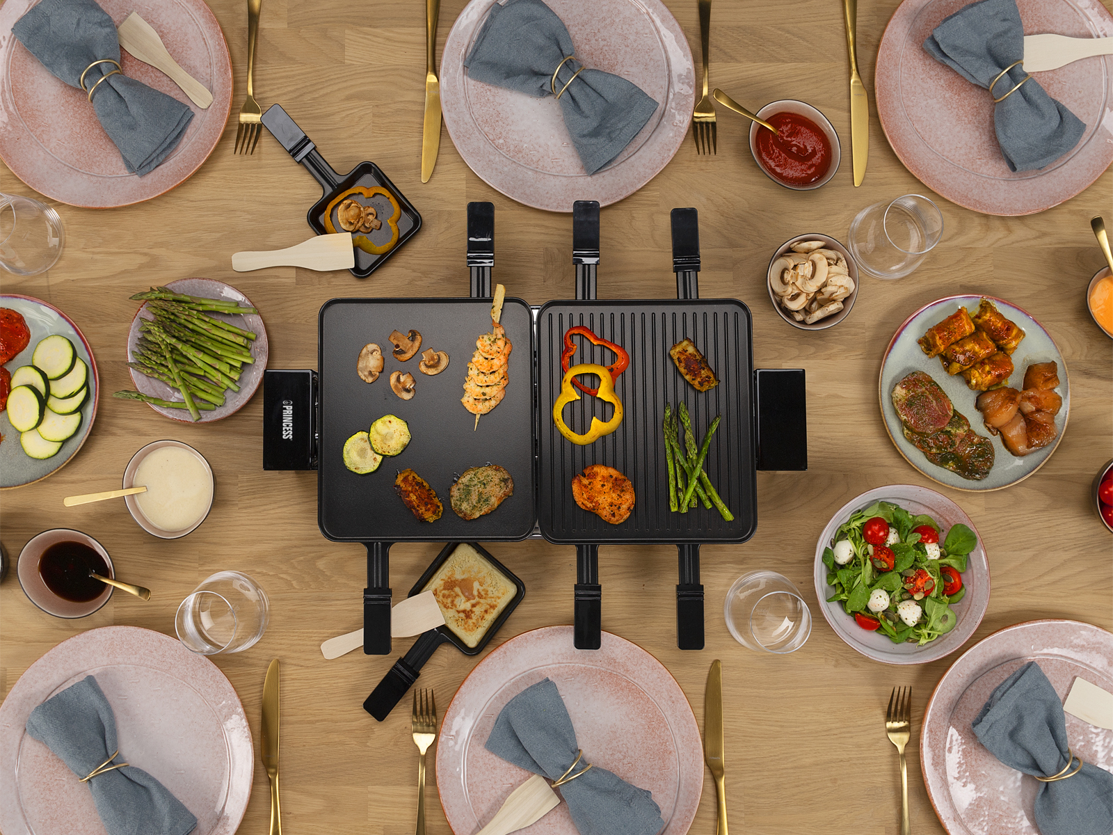 Tischausstattung mit Speisen, darunter gegrilltes Gemüse, Salate und Soßen. Mehrere Teller, Servietten und Utensilien.