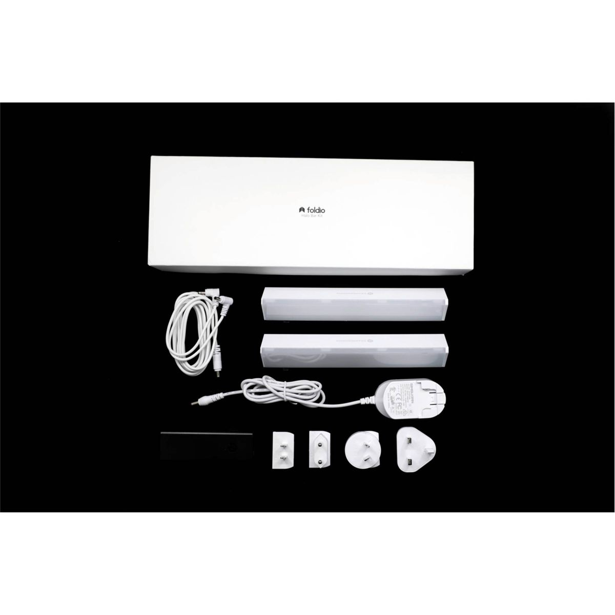 Caja blanca con componentes, cables y enchufes sobre superficie negra.
