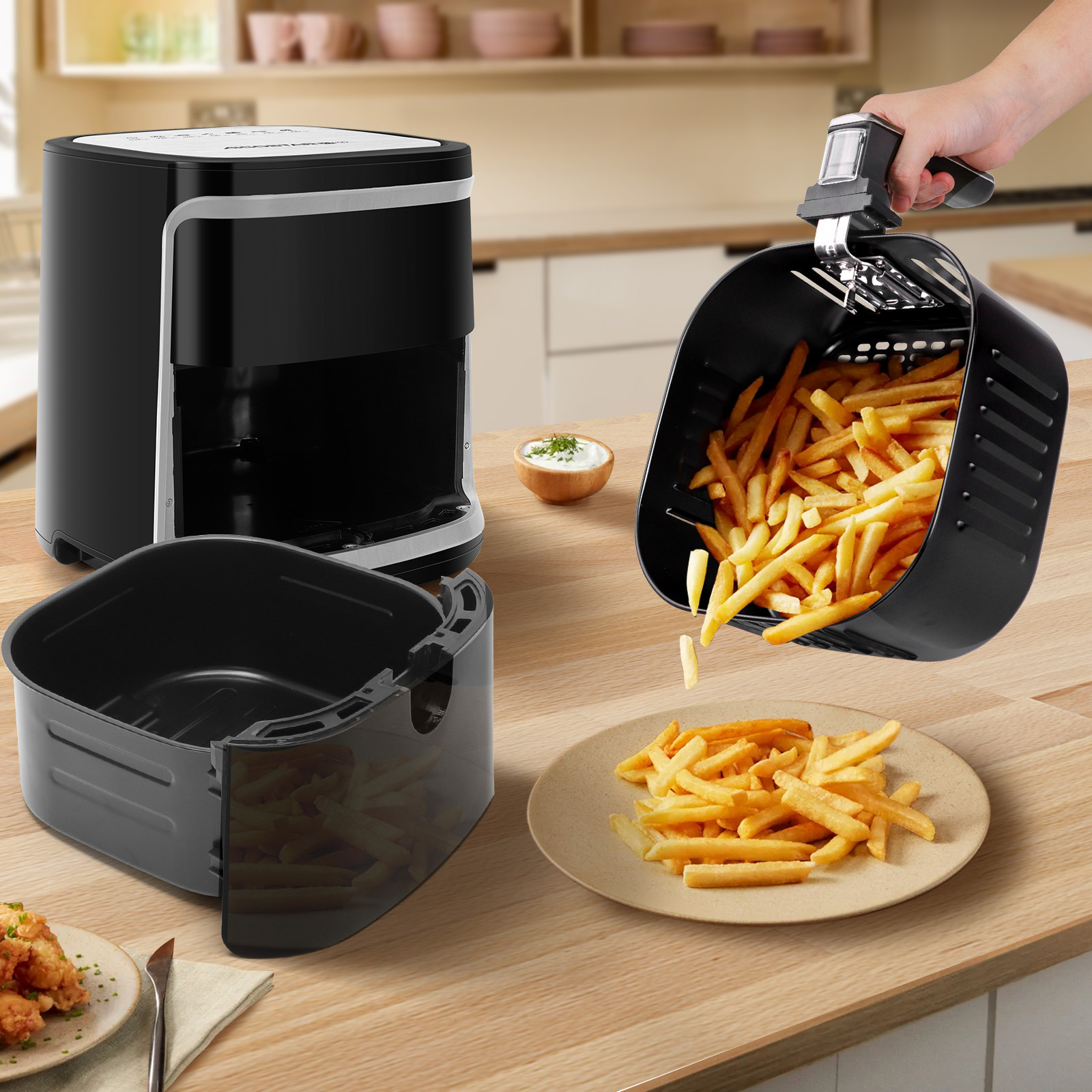 Eine Heißluftfritteuse mit Pommes Frites, einem Teller Pommes Frites und einer Schüssel Soße auf einem Holztisch.