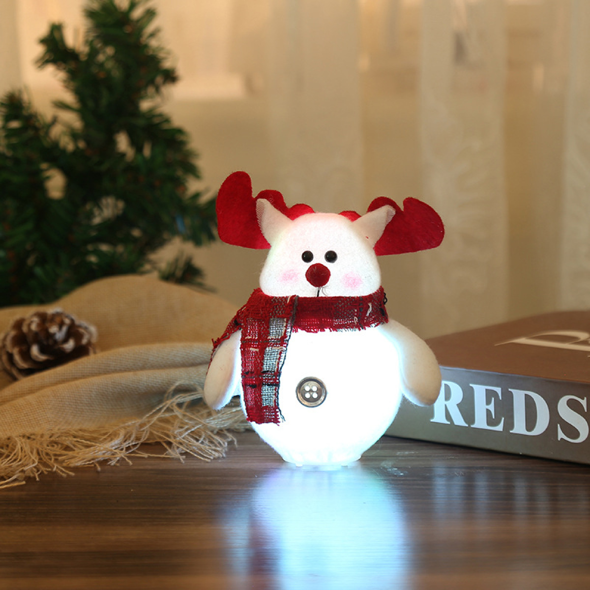Ein beleuchteter Schneemann-Rentier-Hybrid-Weihnachtsschmuck mit Schal und roten Geweihen auf einem Tisch.