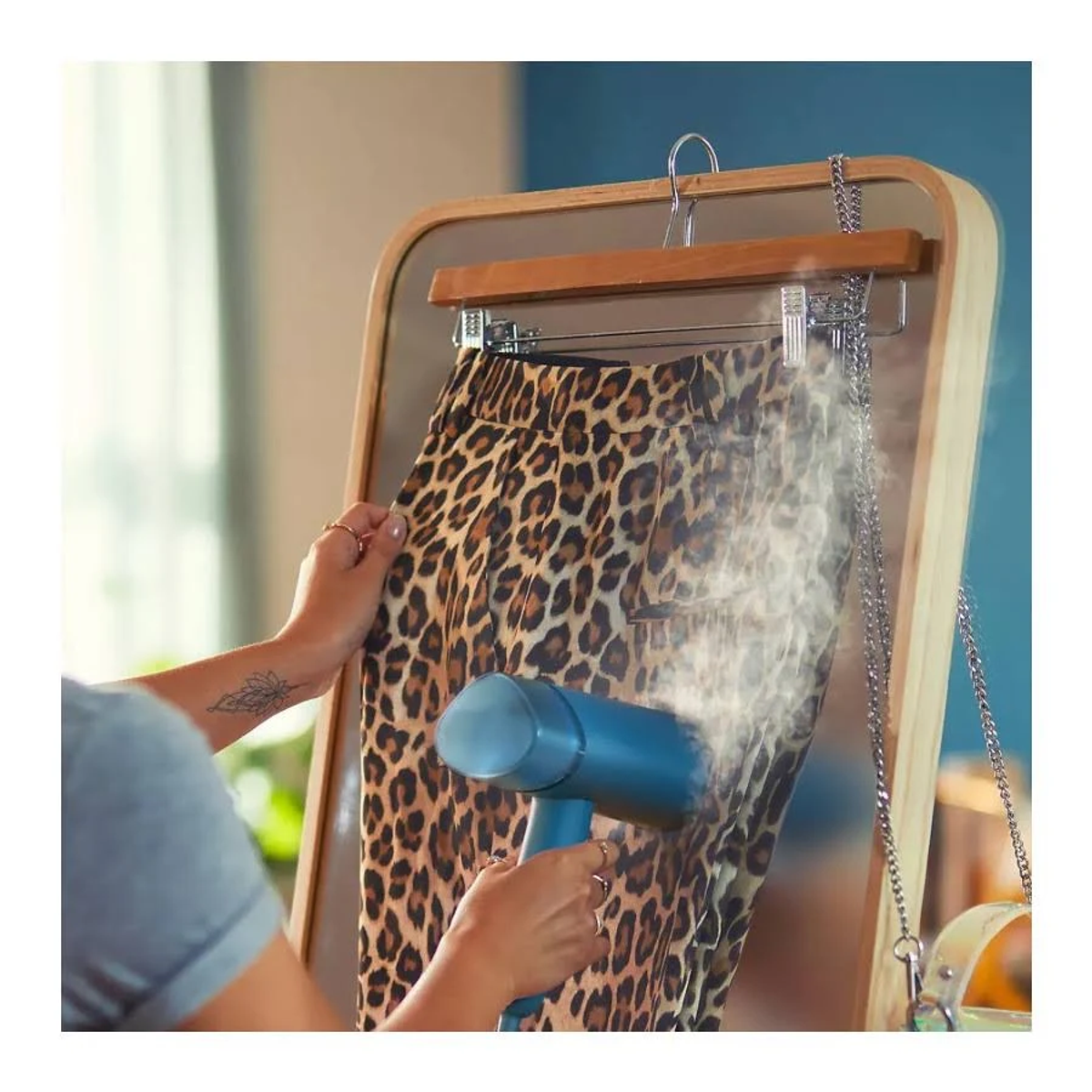 Una mujer planchando con vapor pantalones con estampado de leopardo colgados en un espejo.