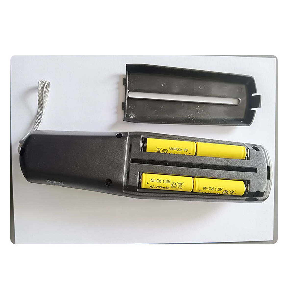 Ein graues Gerät mit zwei gelben Batterien im Inneren. Die Oberseite ist offen. Das Gerät hat eine Schnur befestigt.