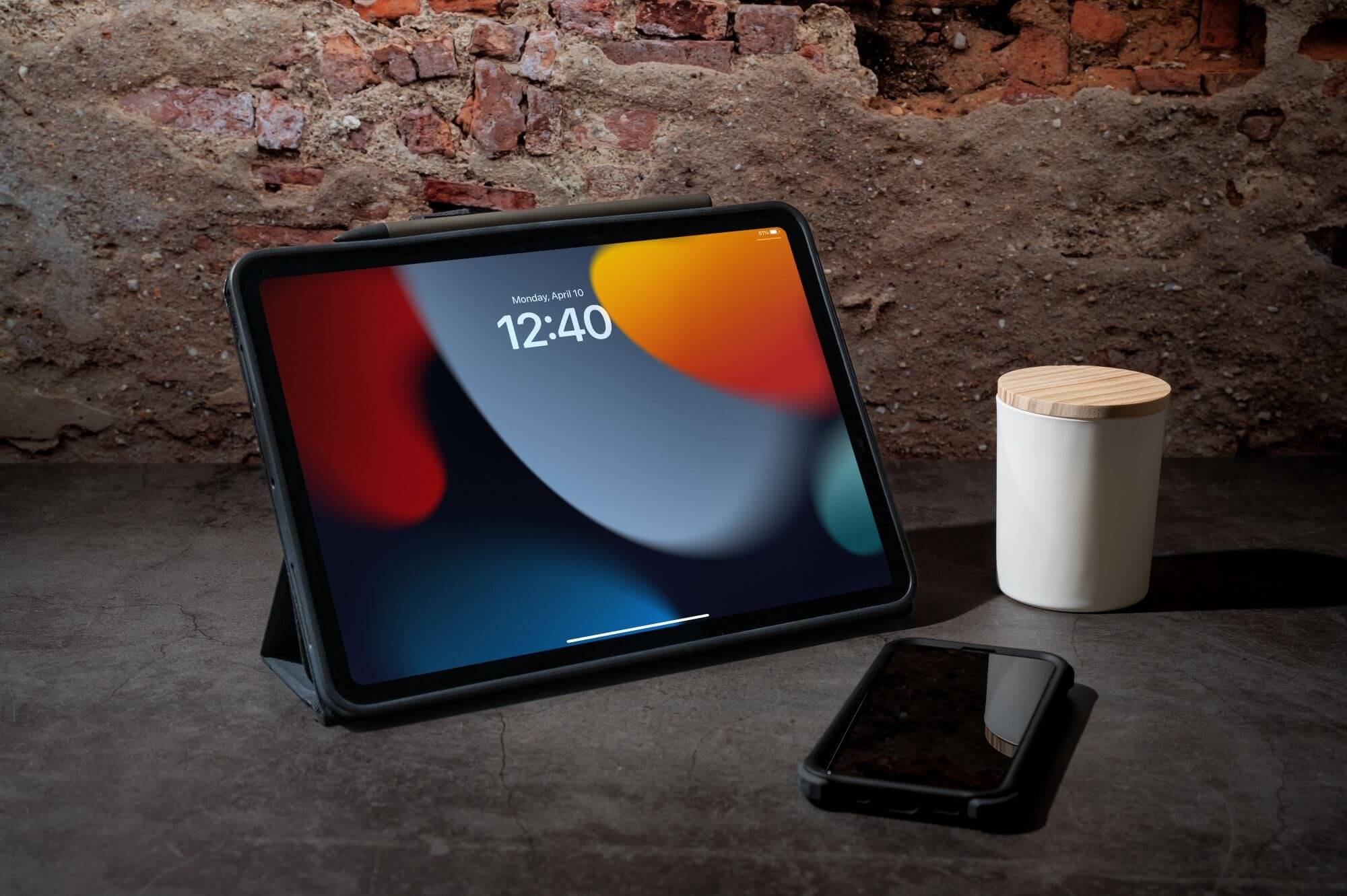 Tablet con custodia scura, su superficie scura. Smartphone e barattolo bianco con coperchio in legno accanto.