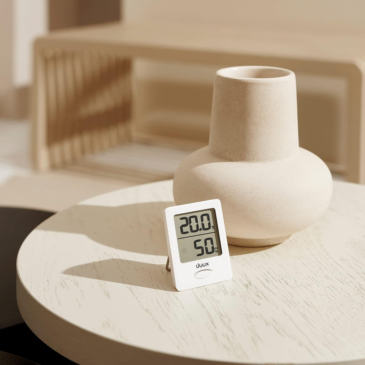 Ein kleines, weißes Digitalthermometer und eine beige Vase auf heller Oberfläche.
