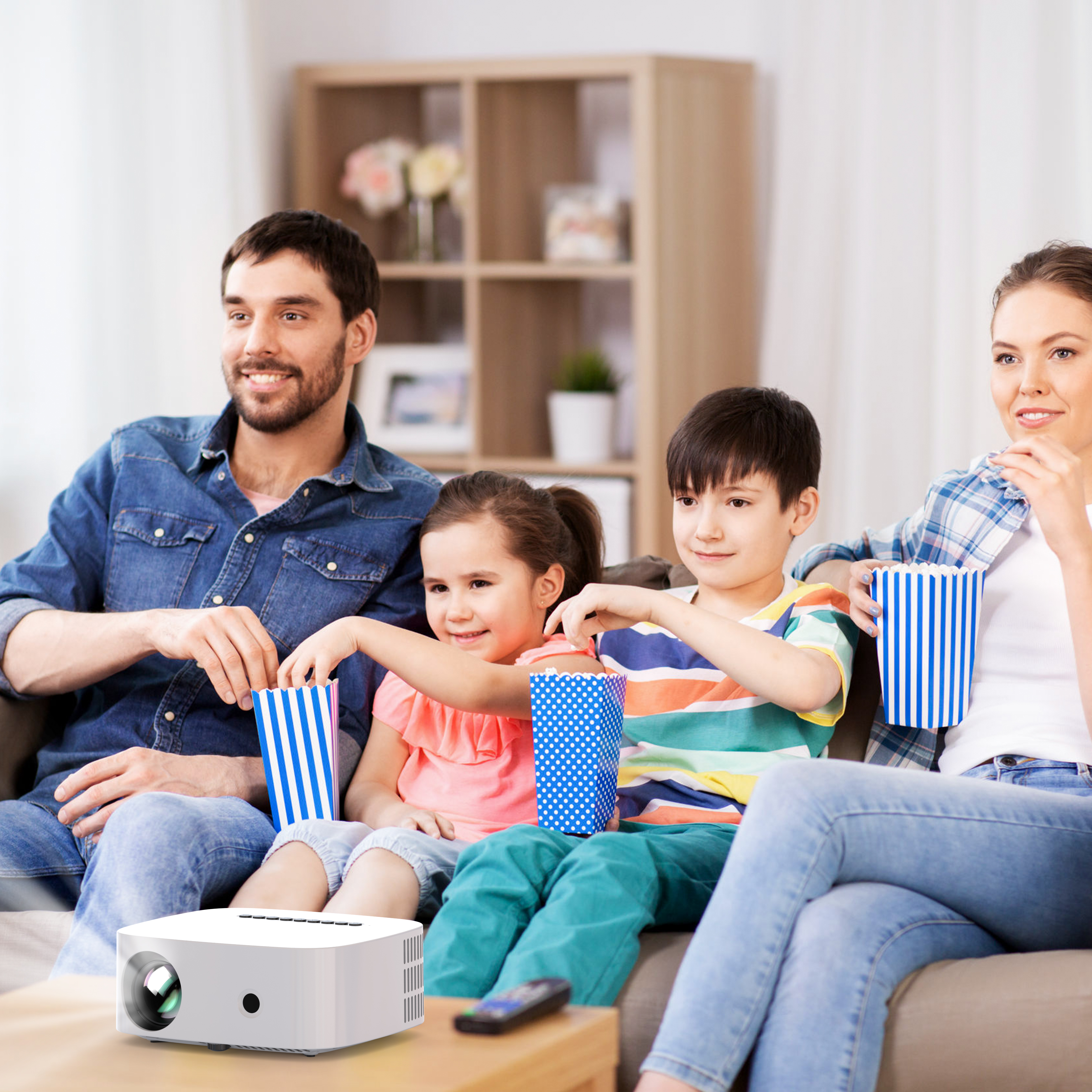 Famille regardant un film avec un projecteur, tenant du pop-corn sur un canapé.