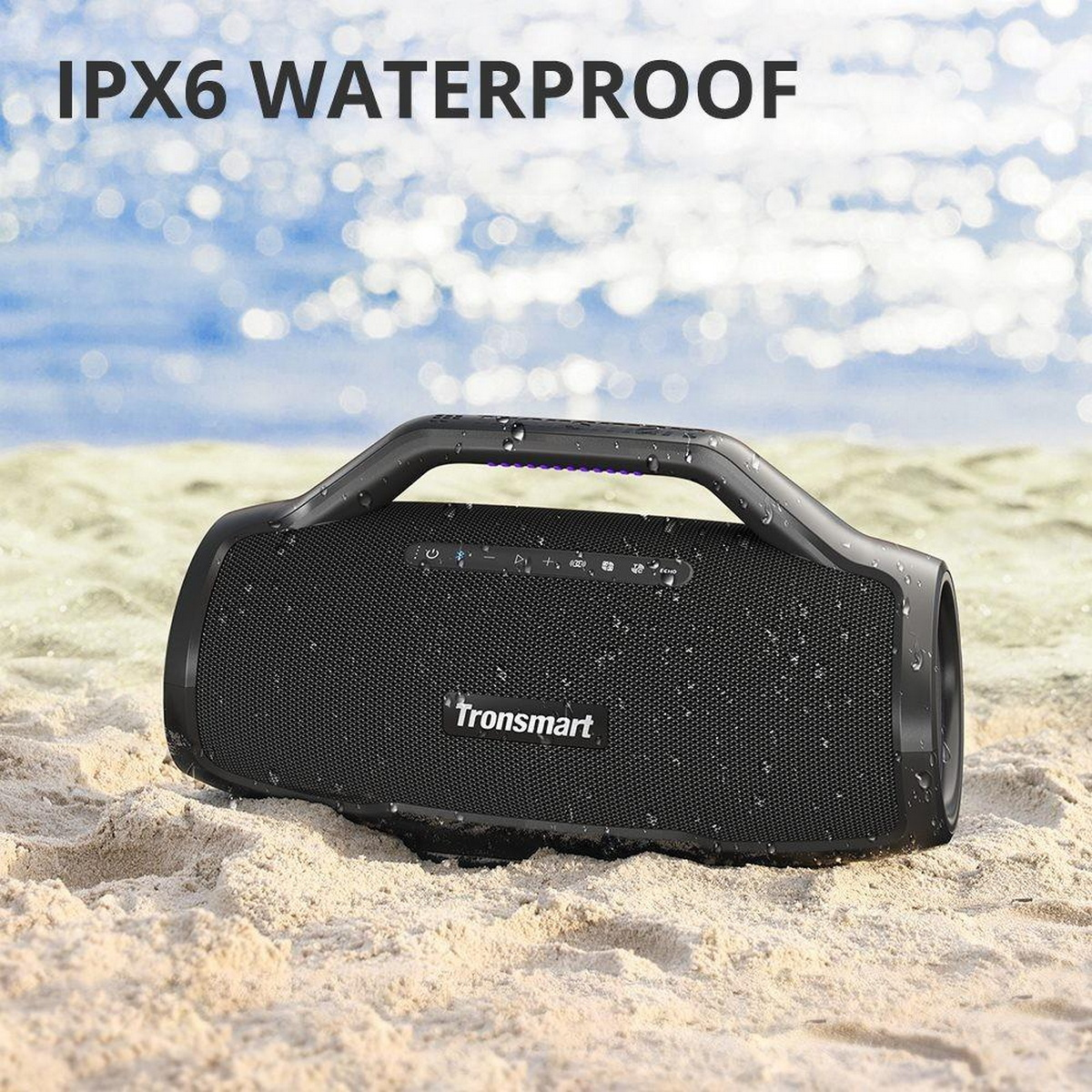 Czarny głośnik Tronsmart na piasku, z kroplami wody. Ma uchwyt i tekst 'IPX6 WATERPROOF'.