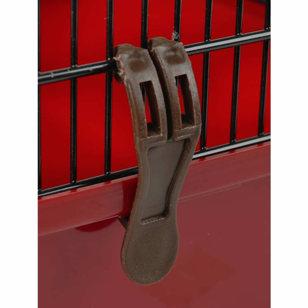 Ein brauner Haustier-Transportkoffer-Verschluss an einem rot-schwarzen Käfig, der den Verriegelungsmechanismus zeigt.