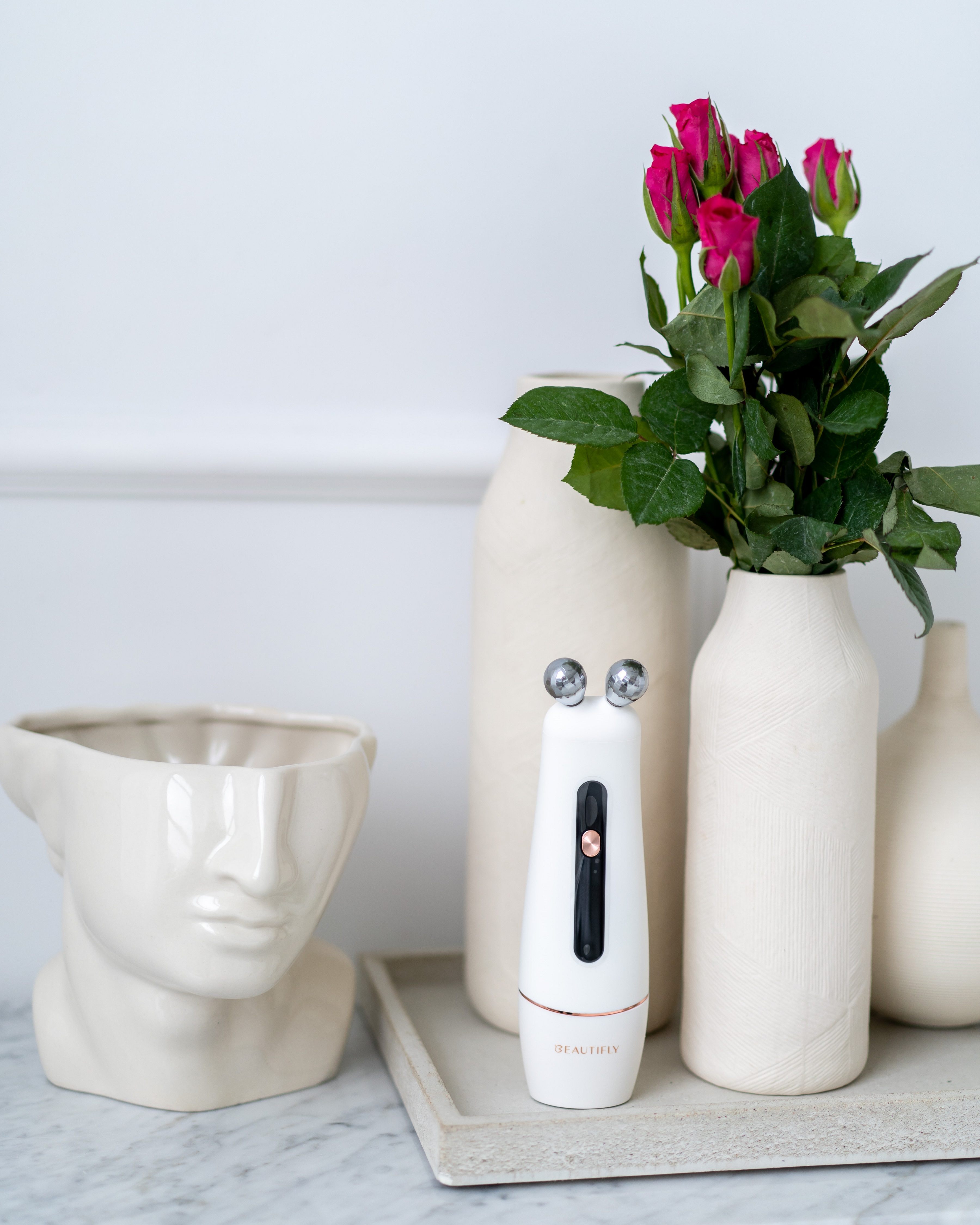 Białe narzędzie kosmetyczne z dwiema kulami, kwiatami w wazonach i rzeźbą. Jasna, estetyczna scena.