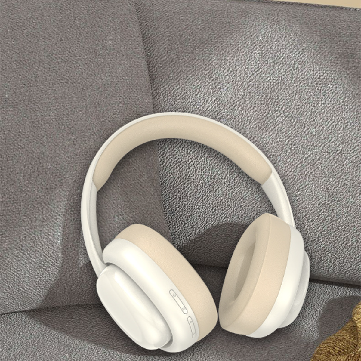 Weiß-beige kabellose Kopfhörer auf einem grauen Sofa. Die Kopfhörer haben einen gebogenen Kopfbügel und große Ohrmuscheln.