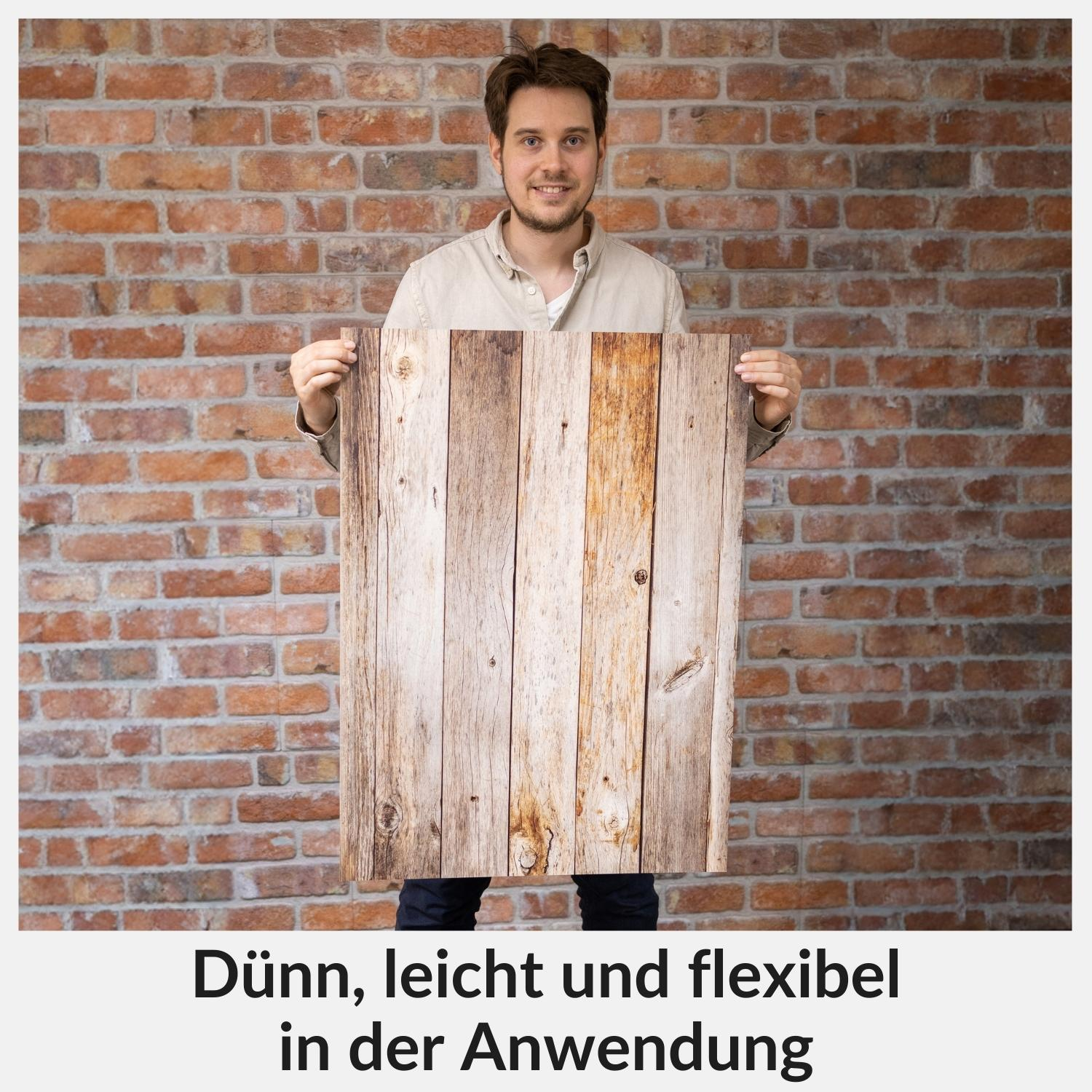 Mann hält Holzpaneel vor einer Backsteinmauer.