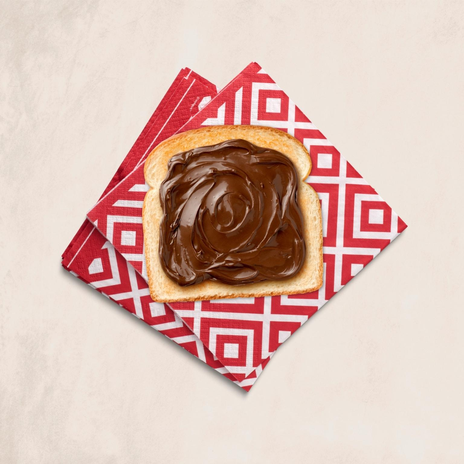 Eine Toastscheibe, bedeckt mit einer dicken Schicht Schokoladenaufstrich, auf einer gemusterten Serviette.