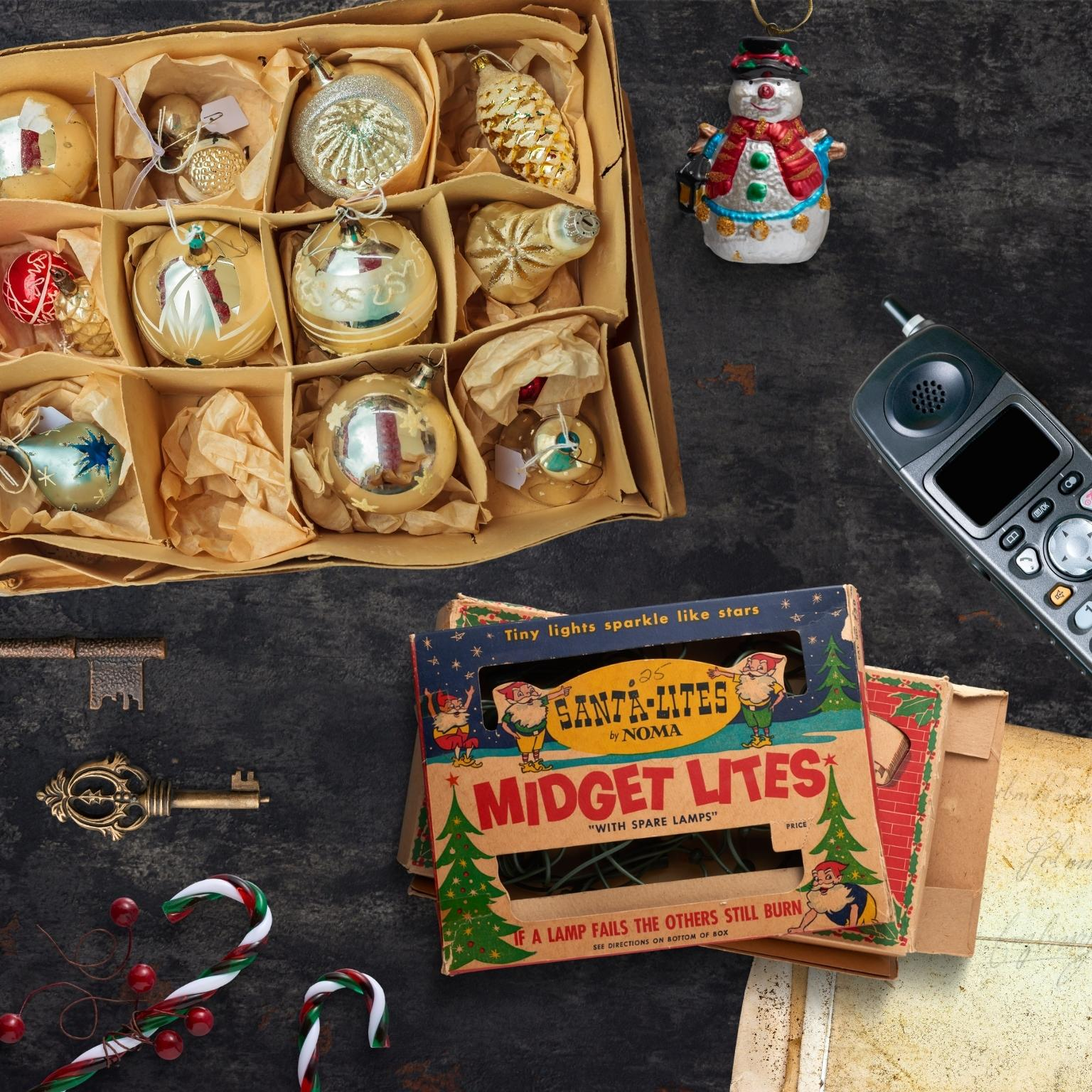 Eine Schachtel mit Weihnachtsschmuck, eine Schneemannfigur, ein Vintage-Telefon, Schlüssel und Zuckerstangen auf einem Tisch.