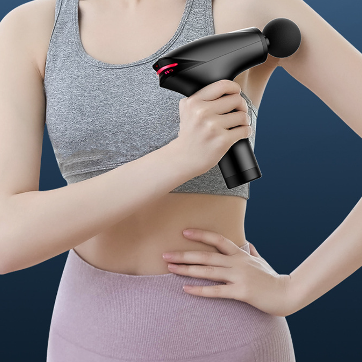 Person hält eine schwarze Massagepistole am Arm, mit grauem Tanktop.