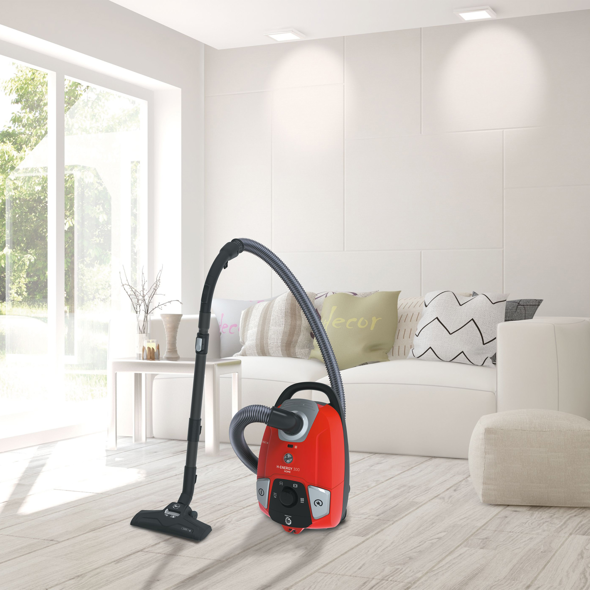 Czerwony odkurzacz z czarnym wężem i dyszą stoi na jasnej drewnianej podłodze w nowoczesnym salonie.