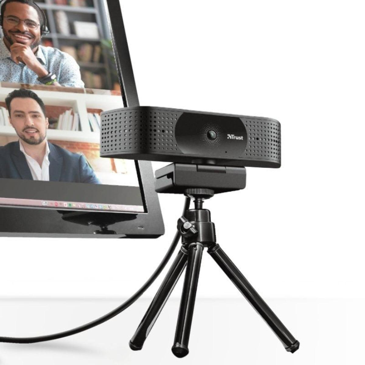 Cámara web en trípode, pantalla con videollamada. Dos hombres en pantalla; uno sonriendo. Cámara negra.