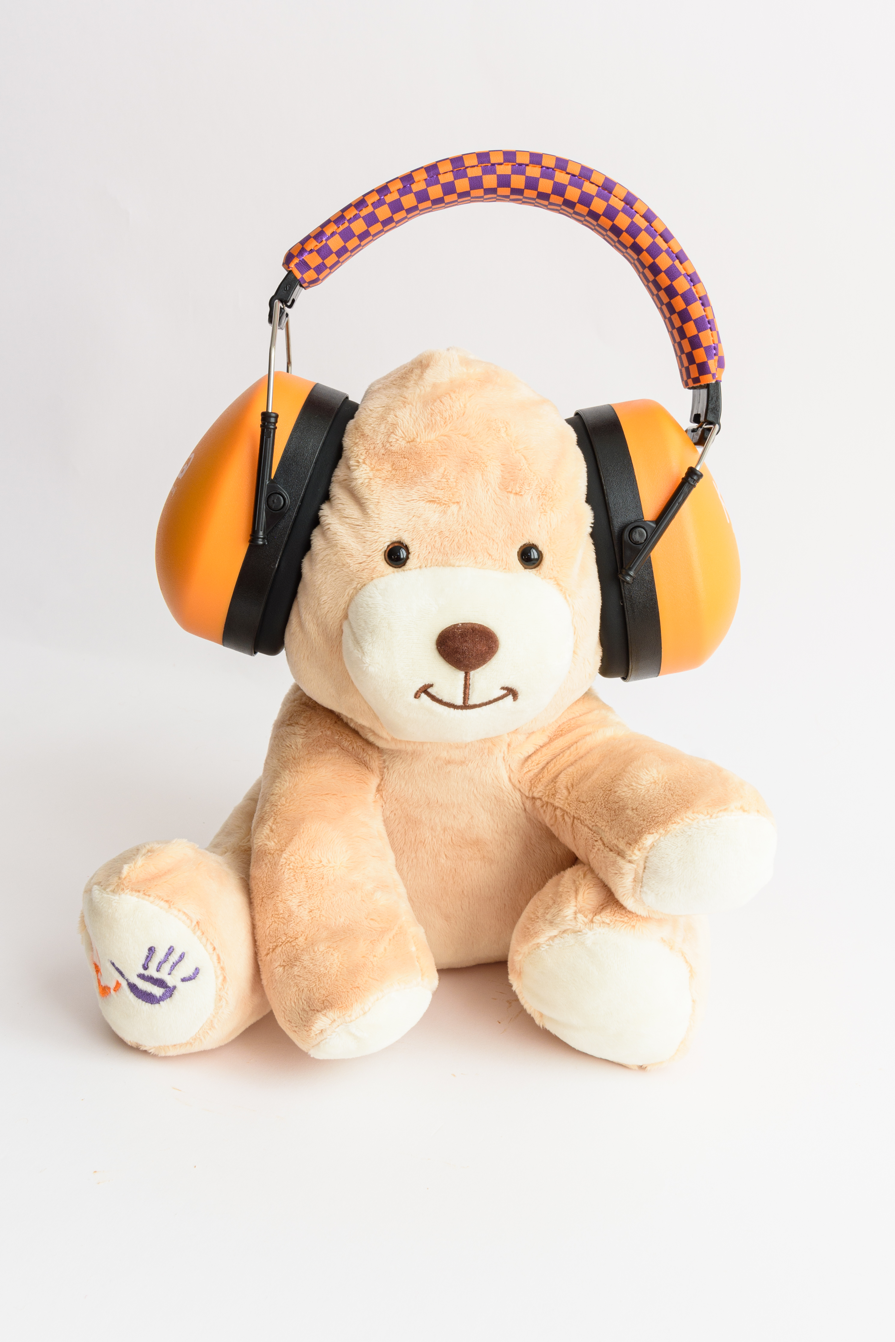 Een teddybeer met oranje gehoorbeschermers en een paars en oranje geruite hoofdband.