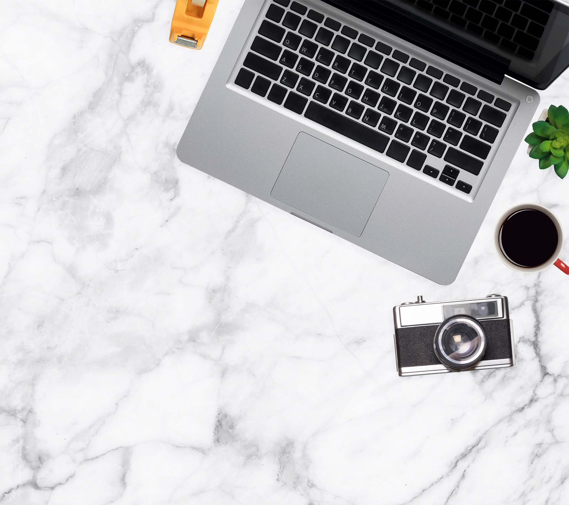 Laptop, Kamera, Kaffee, Klebebandspender und Pflanze auf Marmoroberfläche, Draufsicht.