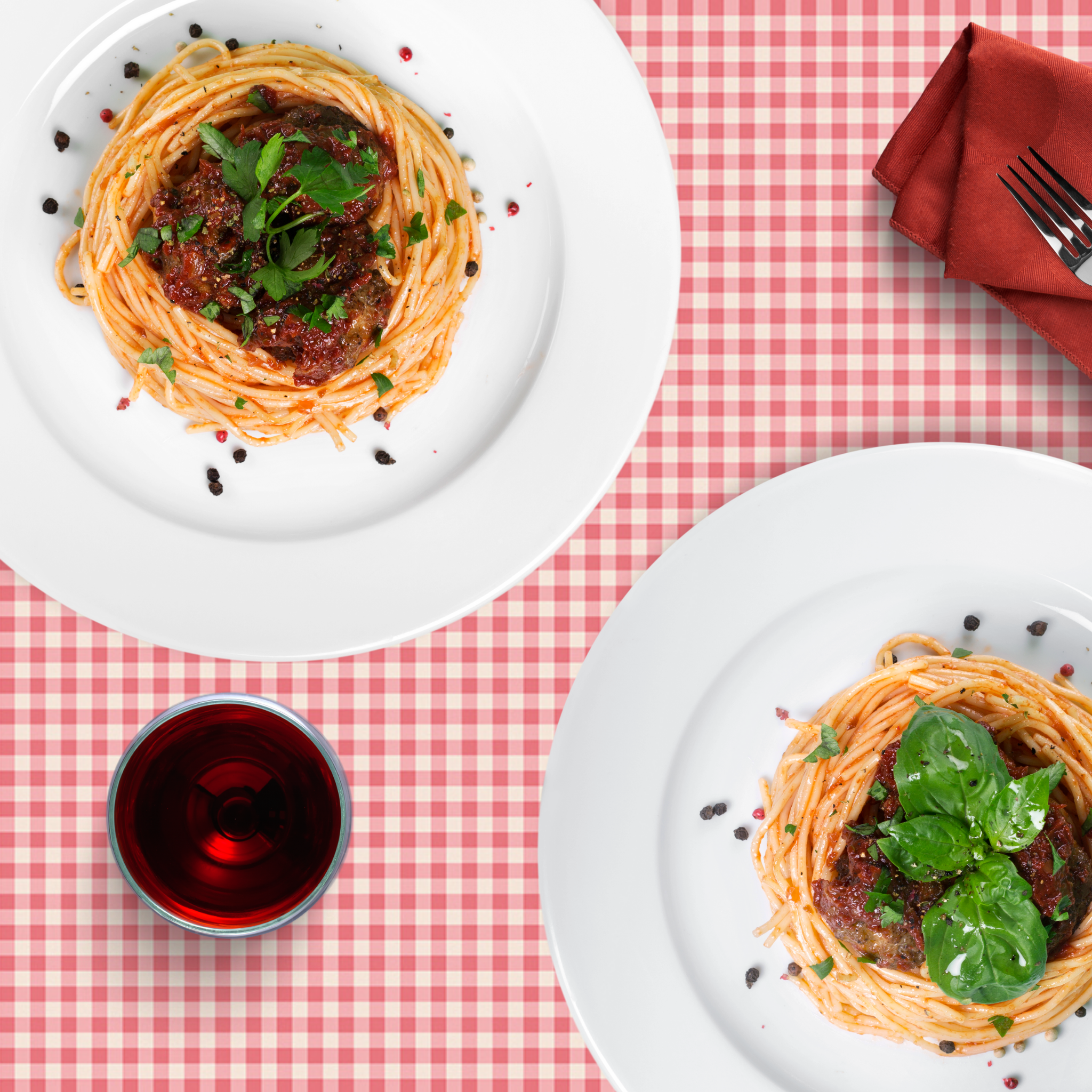 Zwei Teller Spaghetti mit Fleischbällchen und roter Soße, serviert auf einer karierten Tischdecke.