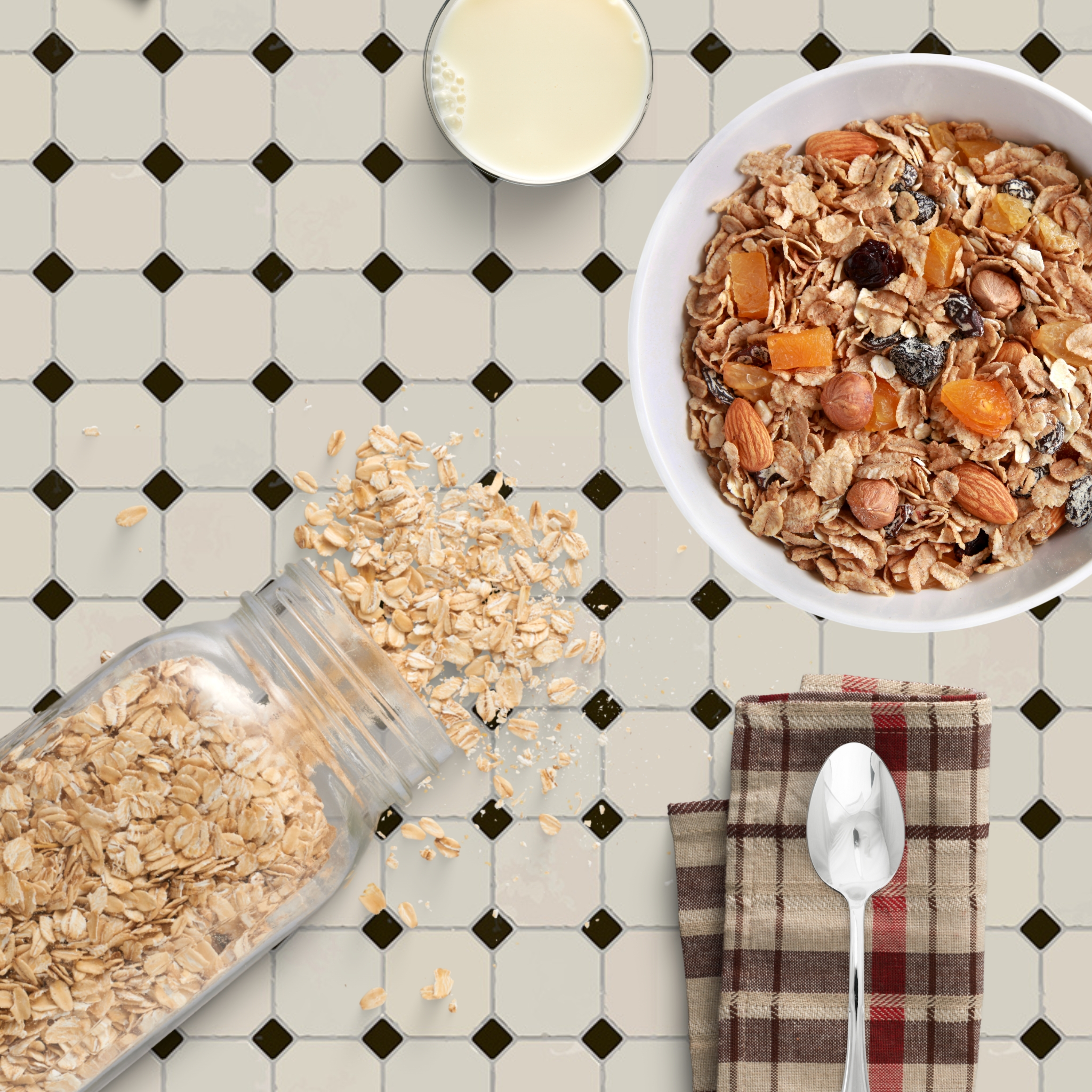 Draufsicht auf Frühstück mit Müsli, Milch, Haferflocken, Löffel und Tuch auf Fliesen.