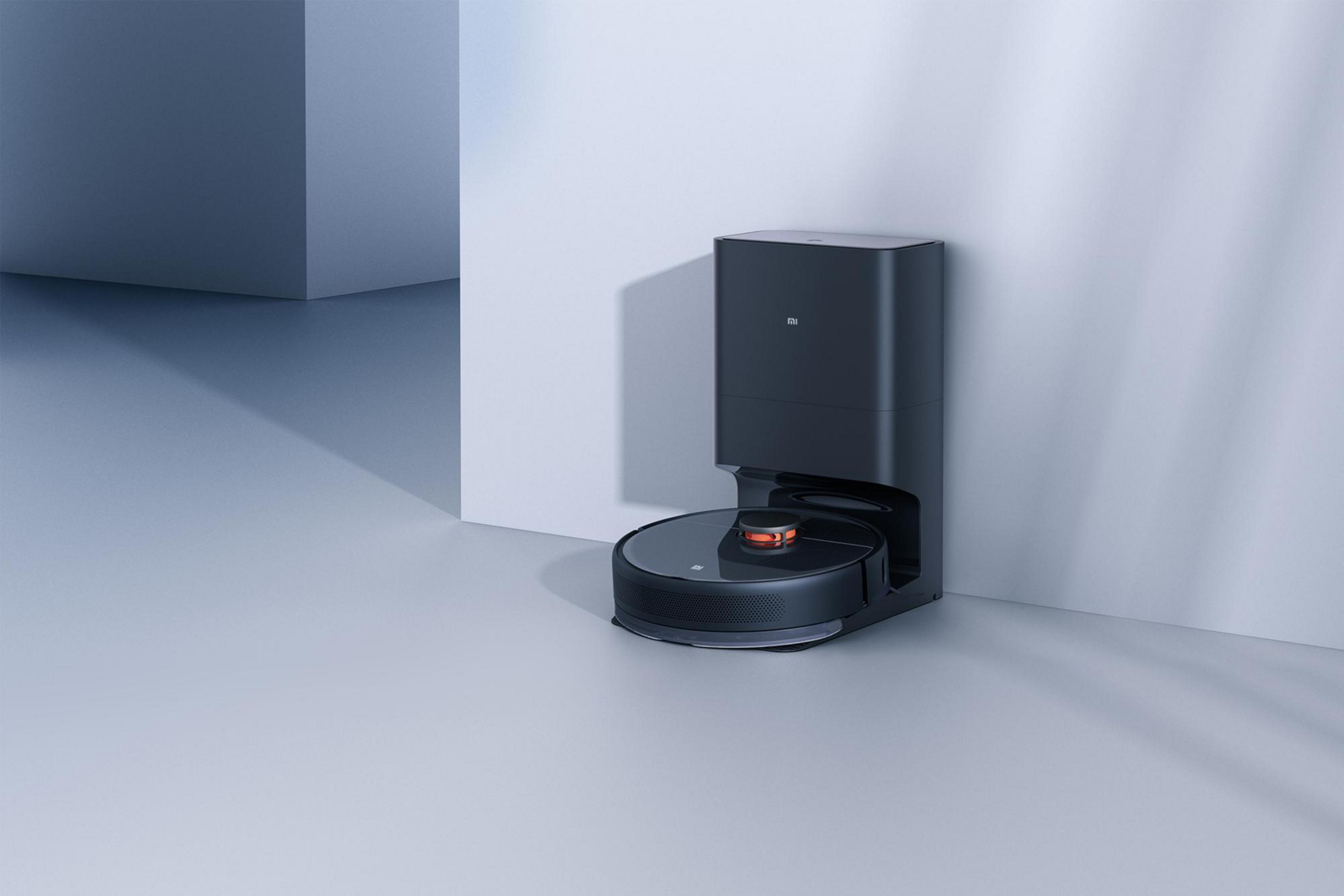 Schwarzer Roboter-Staubsauger mit Ladestation neben einer weißen Wand.
