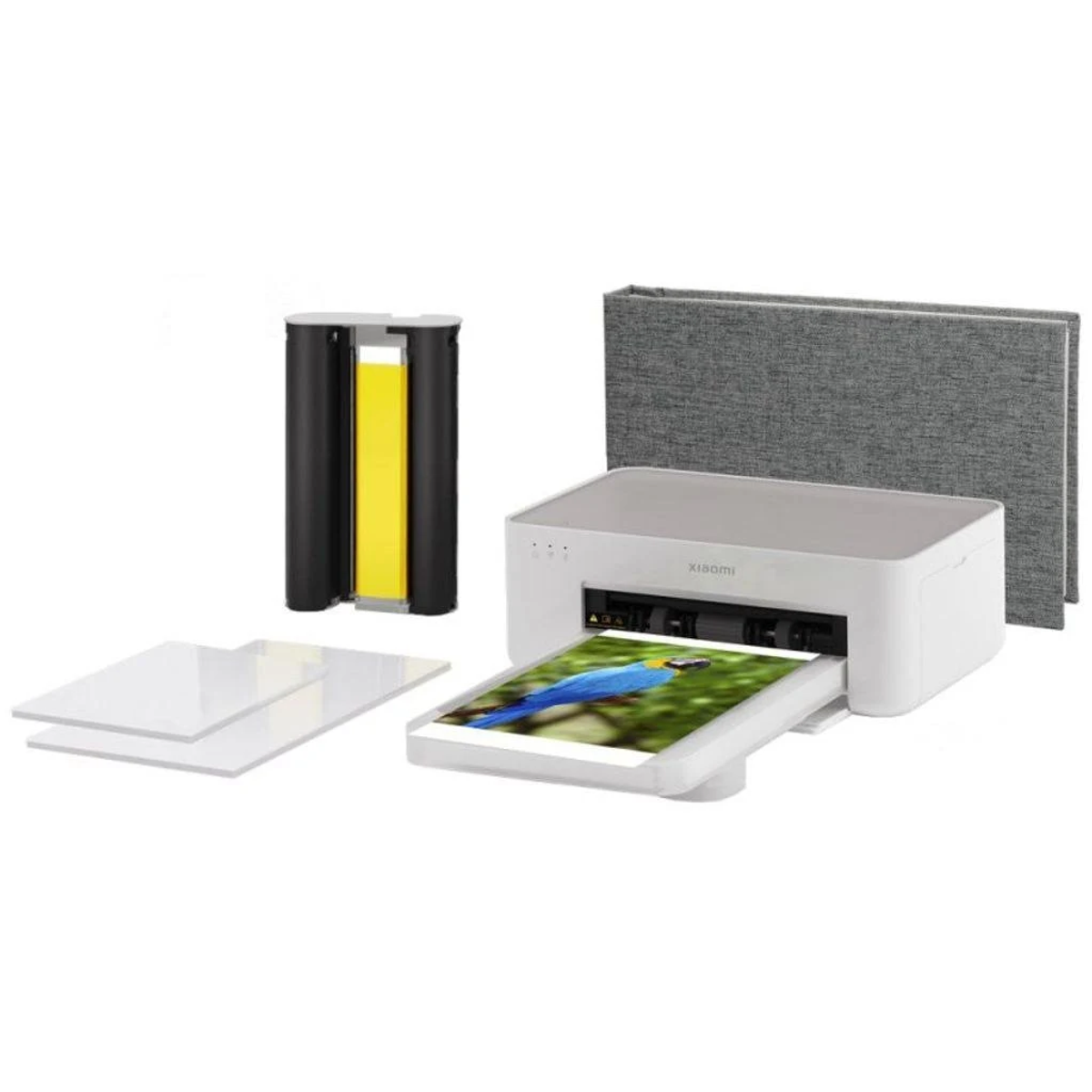 Biała drukarka ze zdjęciem w trakcie drukowania. Dodatki: szara książka, czarny pojemnik i dwa arkusze.