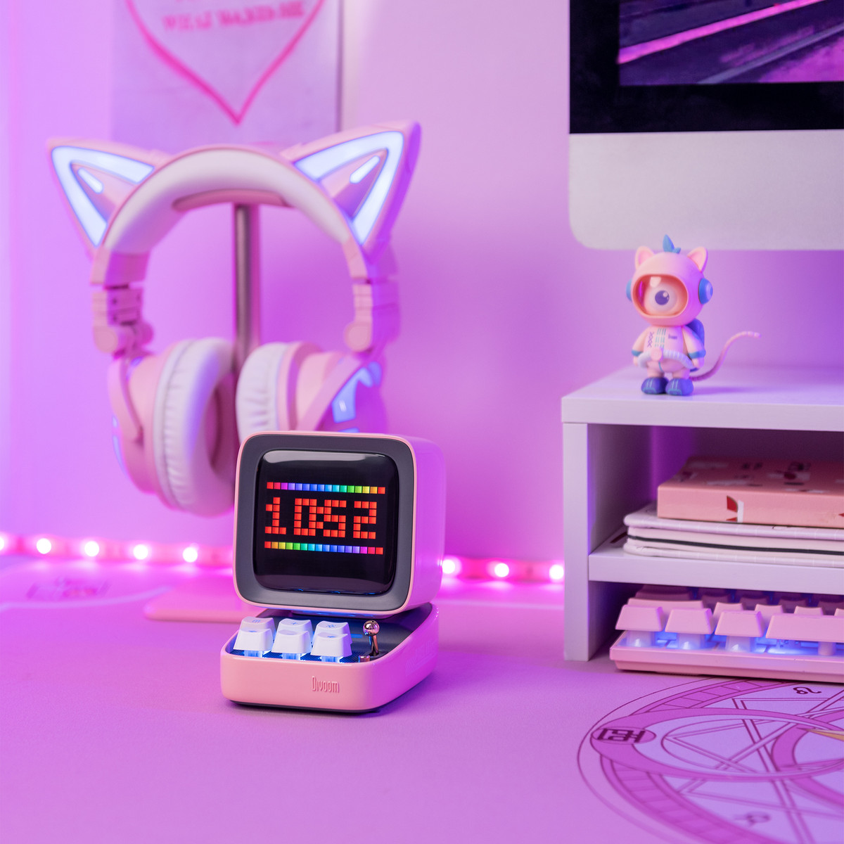 Un altoparlante rosa con un display retrò che mostra l'ora. Cuffie, una tastiera e altri oggetti sono su una scrivania.