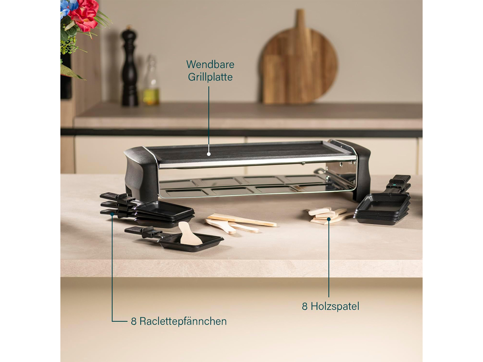 Grill do raclette z patelniami, szpatułkami i drewnianymi akcentami na stole z dekoracją kuchenną.
