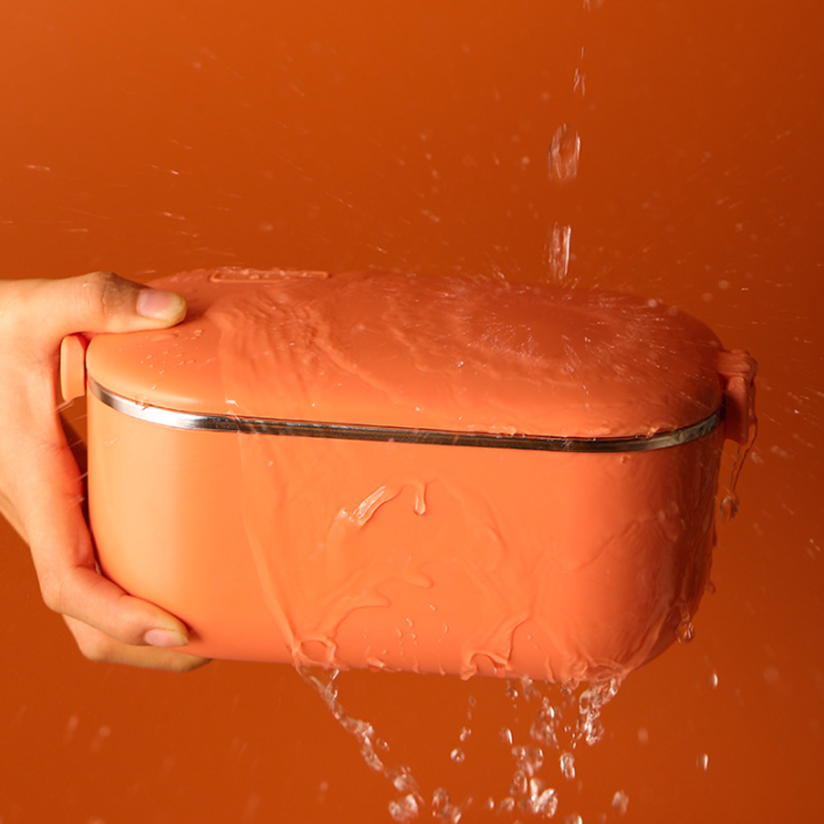 Eine orangefarbene Brotdose wird mit Wasser bespritzt, wobei Wassertropfen und eine nasse Oberfläche zu sehen sind.