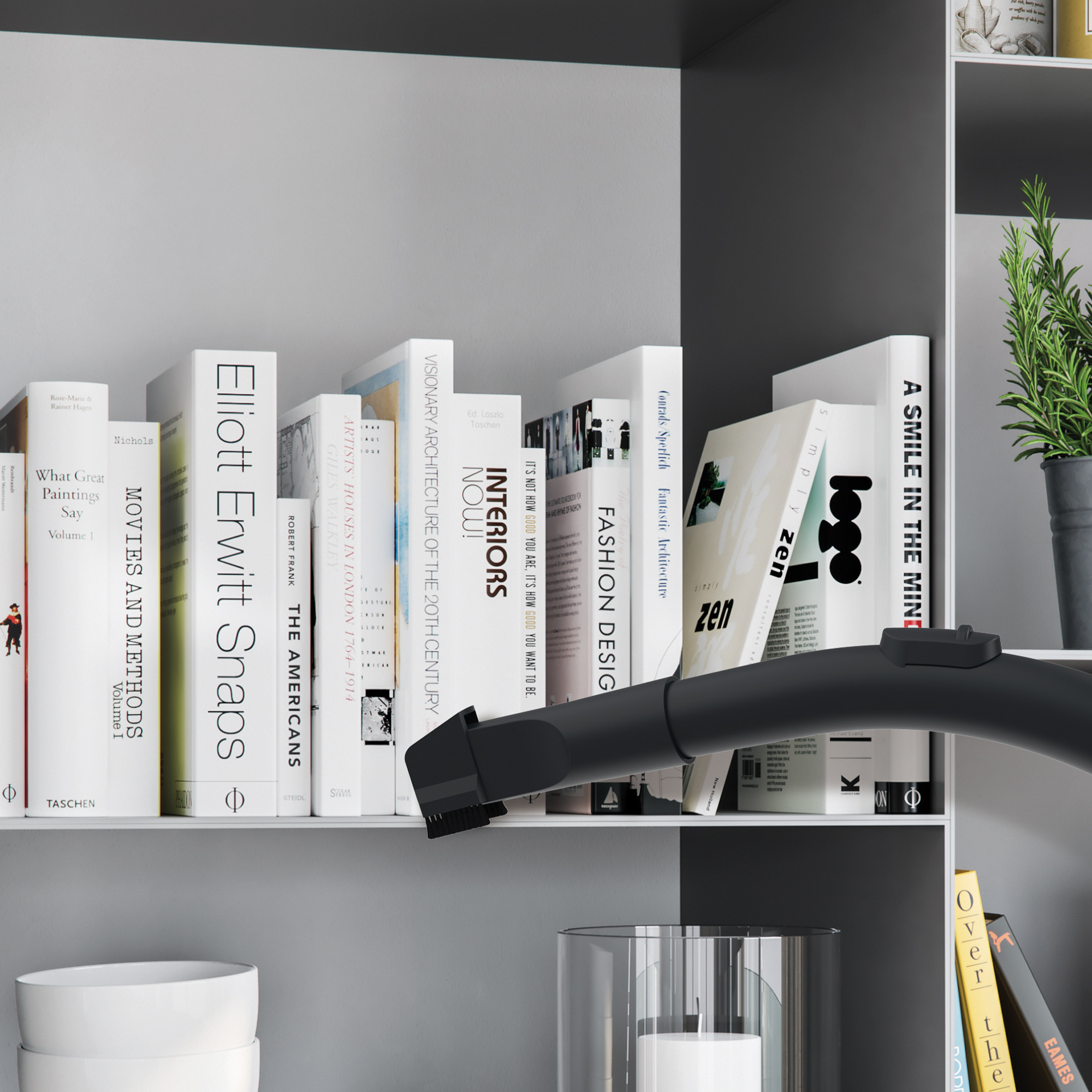 Książki na półce czyszczone odkurzaczem, z widocznymi białymi miskami.