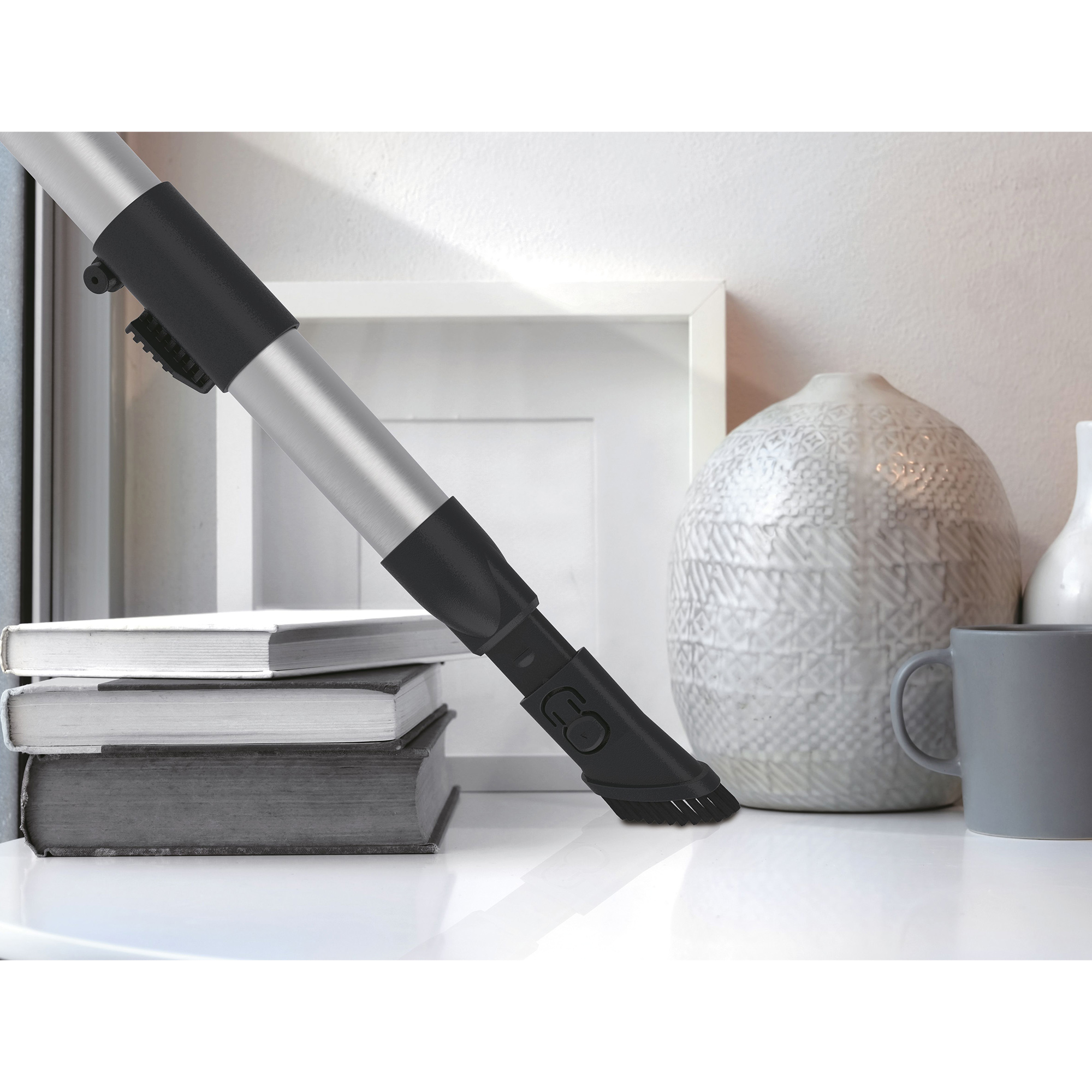 Końcówka odkurzacza czyszcząca białą powierzchnię. Stos książek i kubek w tle.