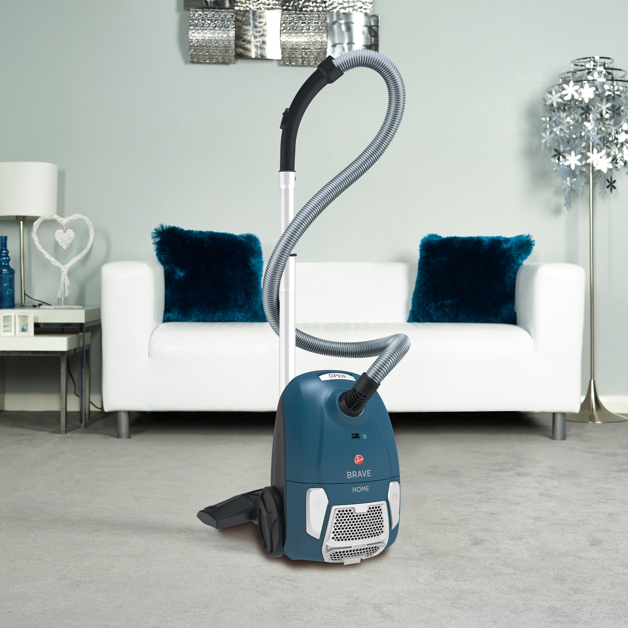 Niebieski odkurzacz ze srebrnym wężem i biała sofa z niebieskimi poduszkami.