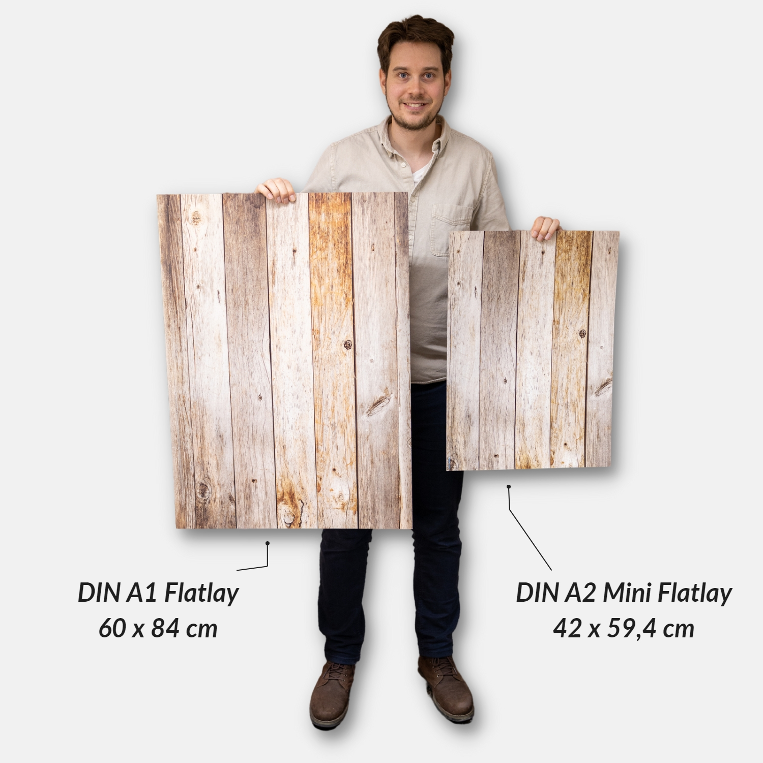 Ein Mann hält zwei Kunstdrucke mit Holzmaserung, beschriftet mit A1 und A2 Größen.