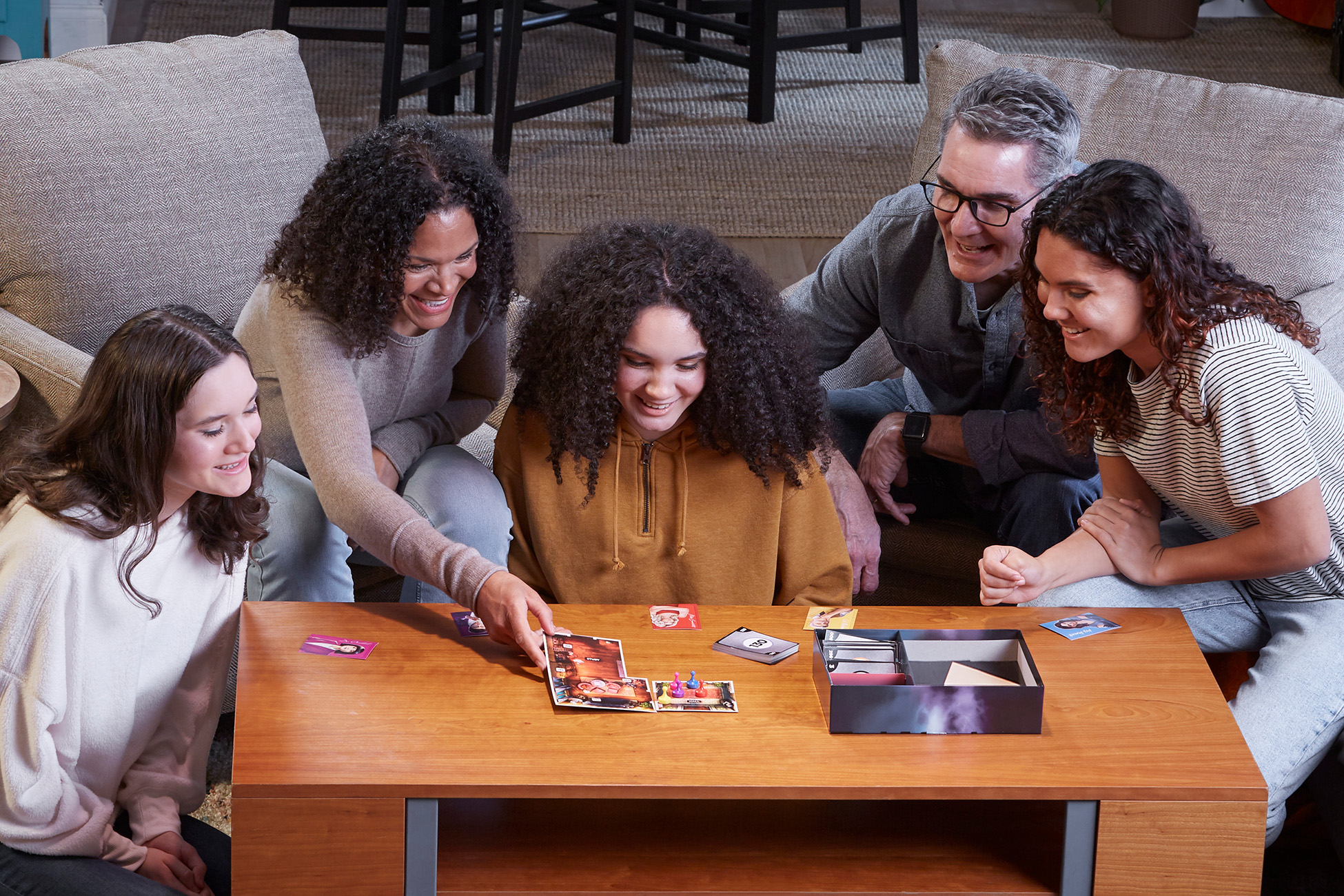 Eine Familie spielt ein Brettspiel. Sie sitzen an einem Holztisch und interagieren mit Spielsteinen.