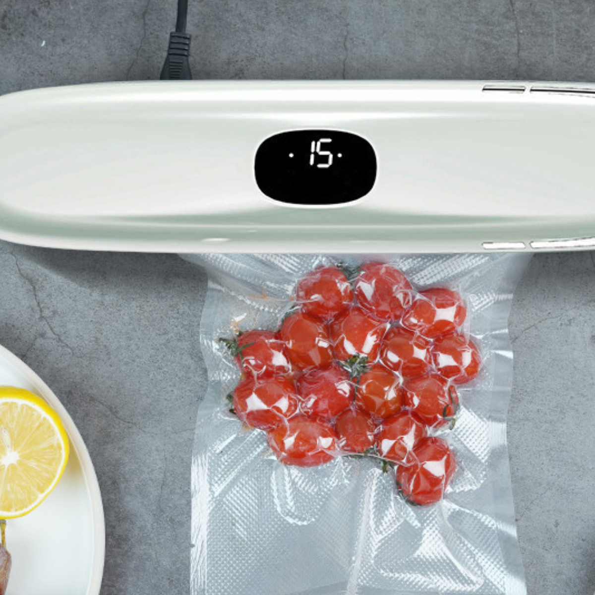 Ein Vakuumierer mit einer Tüte roter Cherrytomaten und einer Zitronenscheibe auf einem Teller.