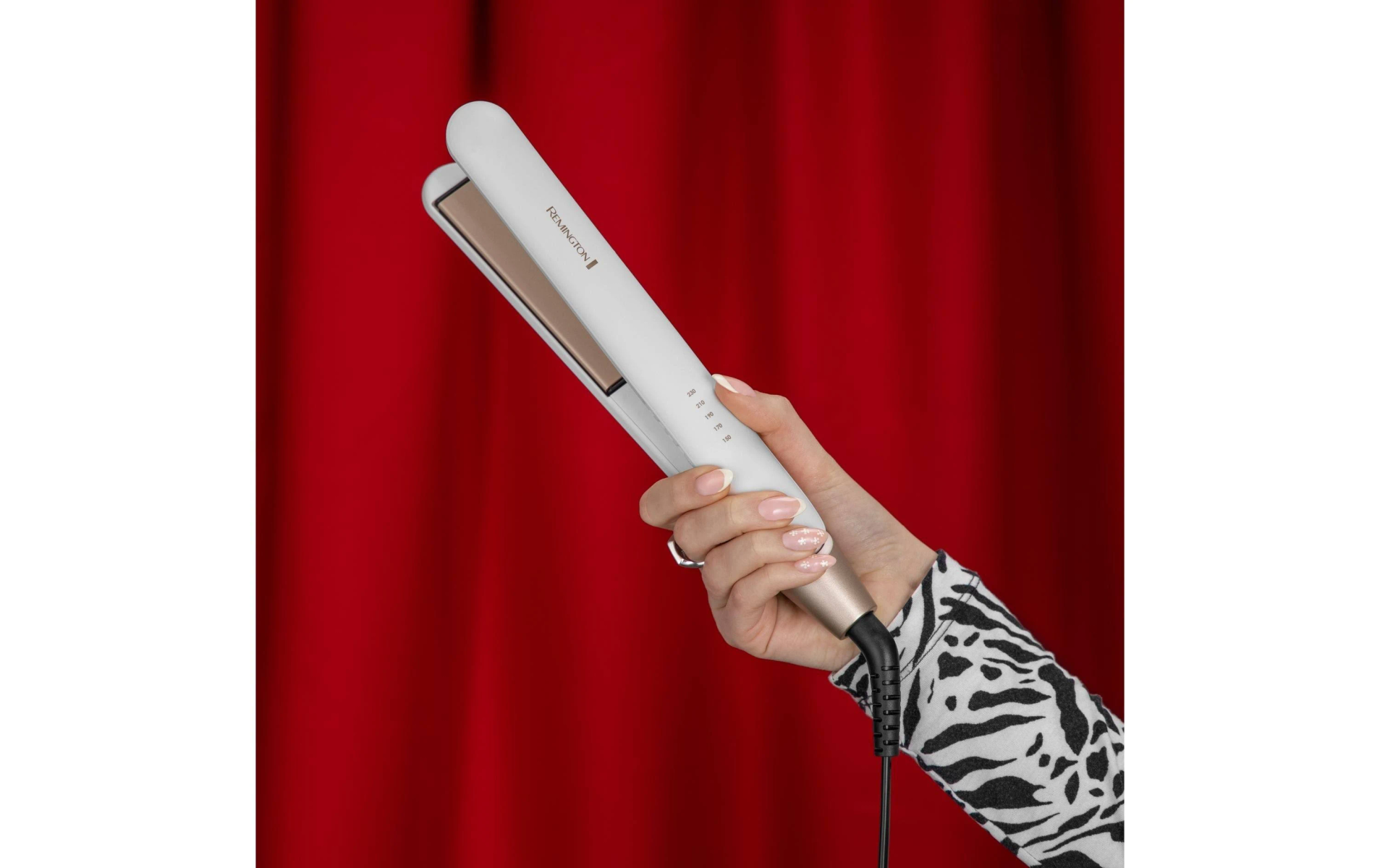 Die Hand einer Frau, die einen weißen Haarglätter vor rotem Hintergrund hält.