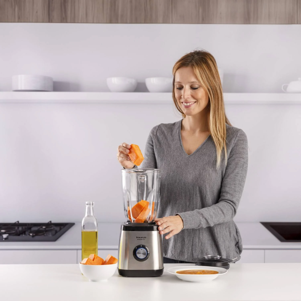Una donna sta frullando pezzi di papaya. È in una cucina. Una bottiglia d'olio è sul bancone.