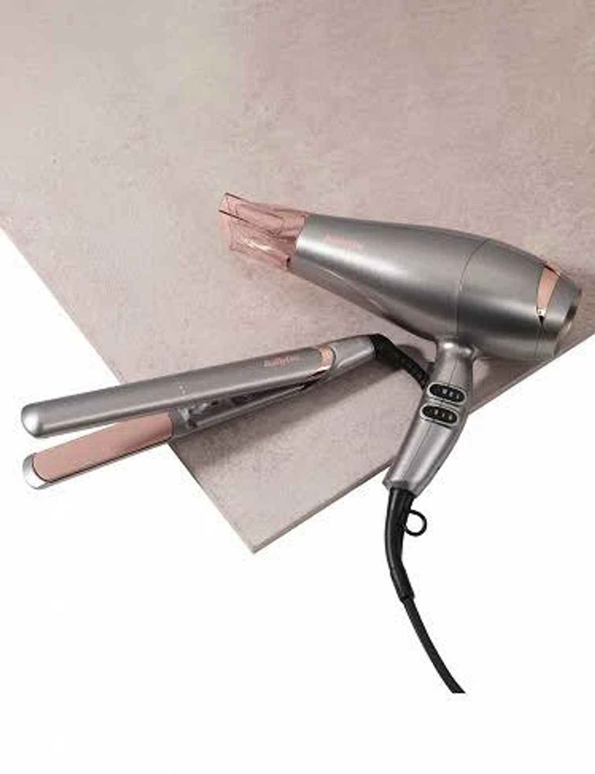 Zestaw suszarki i prostownicy na jasnej powierzchni. Srebrne i różowe akcenty.