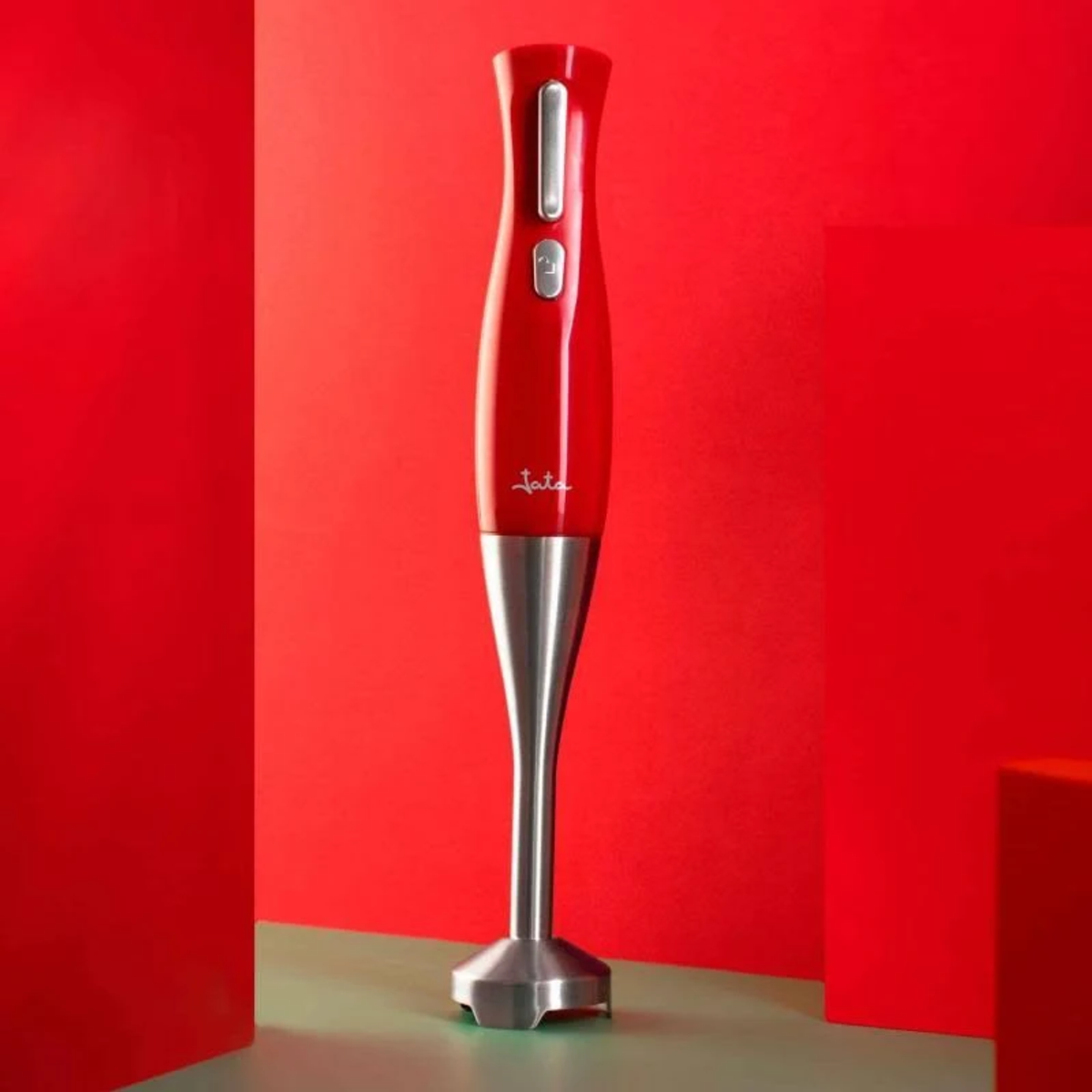 Batidora de mano roja, eje plateado. Fondo rojo con superficie verde.