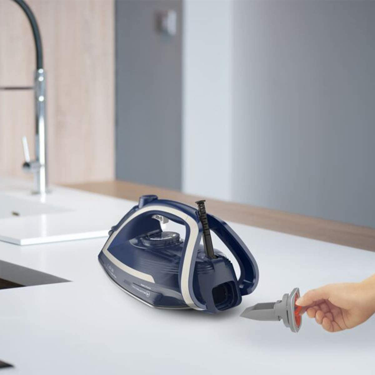 A blue and white iron sits on a white counter. A hand is removing a filter.