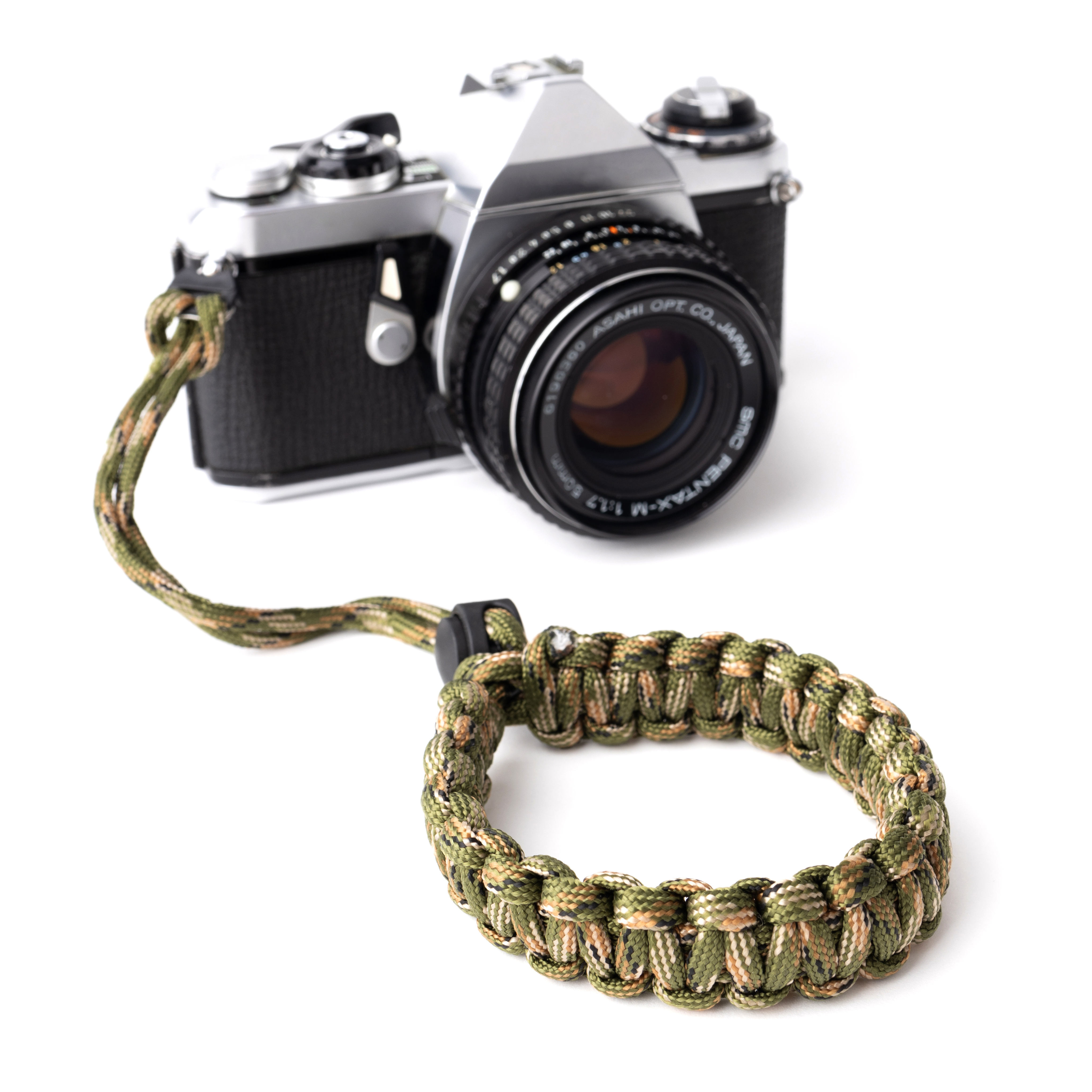 Eine Kamera mit Trageriemen und ein Camouflage-Armband liegen auf weißer Oberfläche.