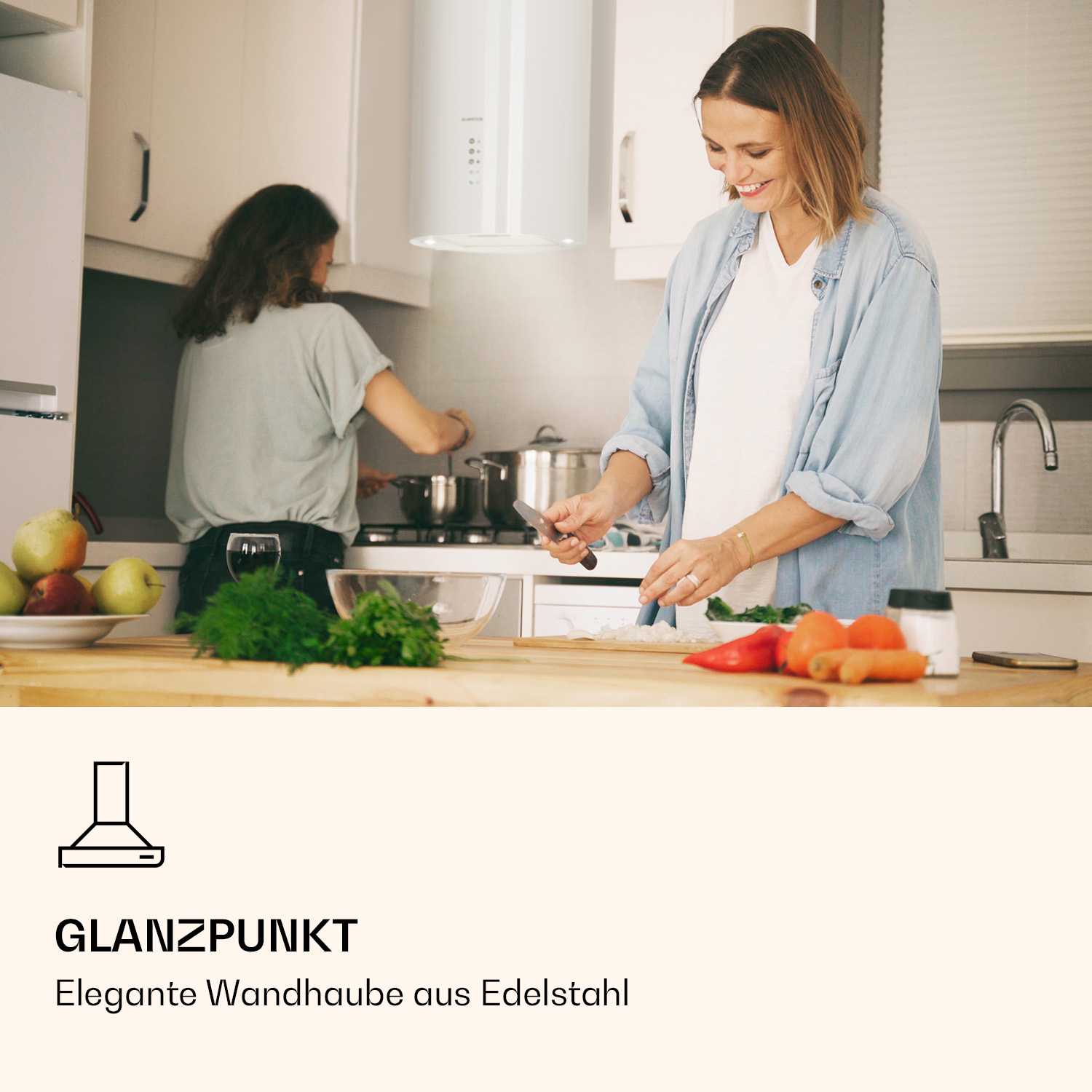Una escena de cocina con dos mujeres, una cortando verduras debajo de una campana extractora blanca.