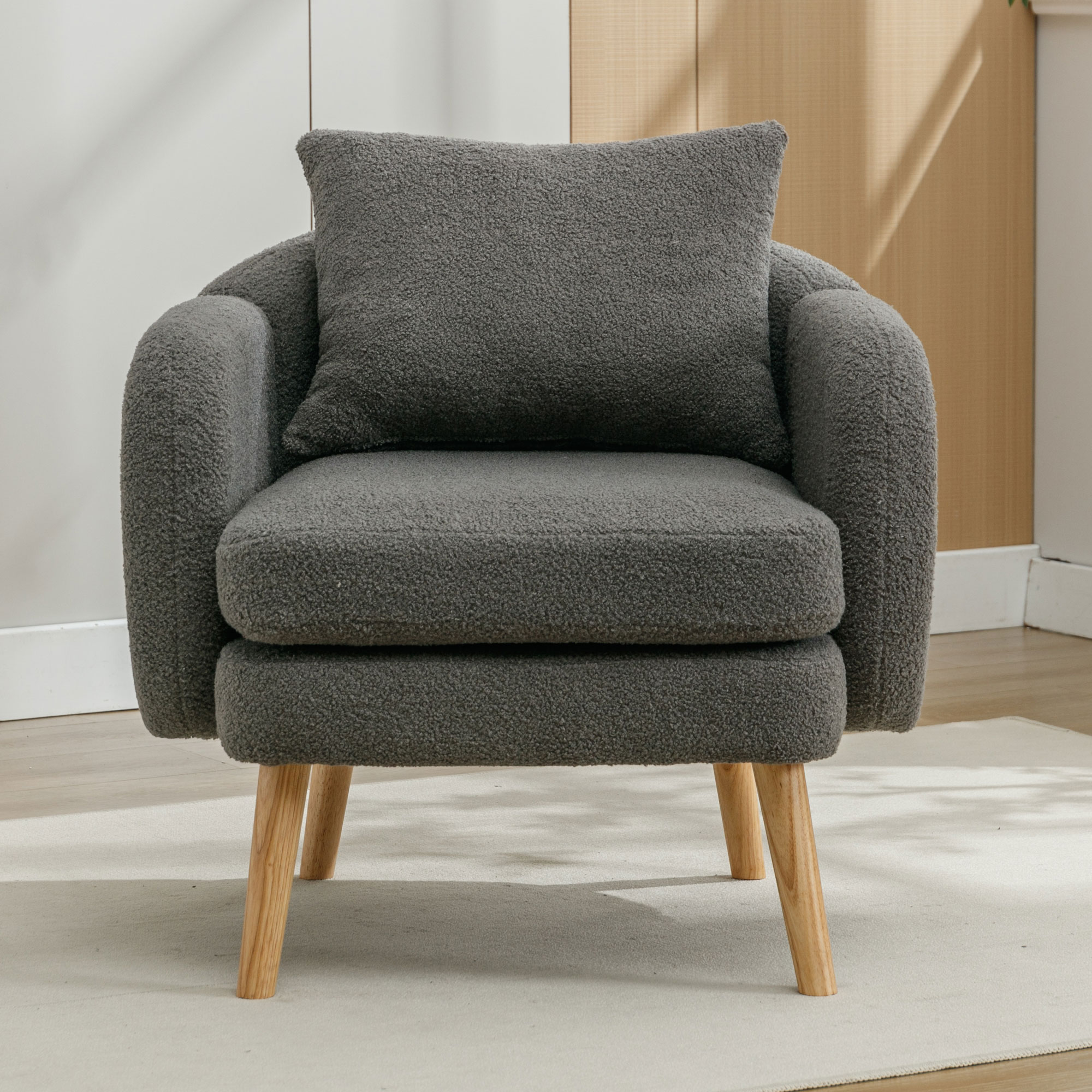 Grauer Sessel mit Kissen auf einem Teppich. Er hat Holzbeine. Im Hintergrund ist eine helle Wand.